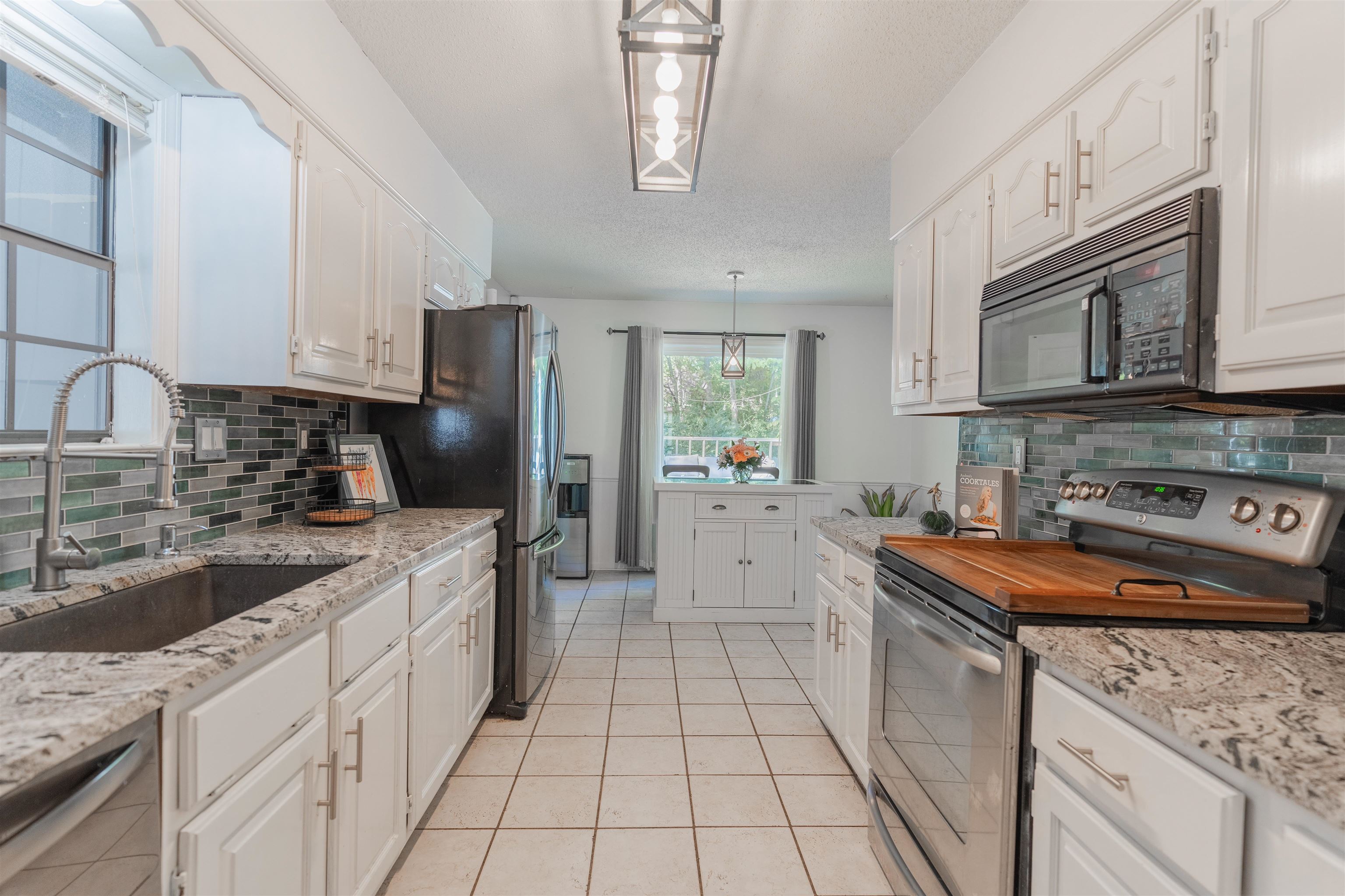 Kitchen featuring hanging light fixtures, stainless steel appliances, sink, light tile patterned floors, and white cabinetry