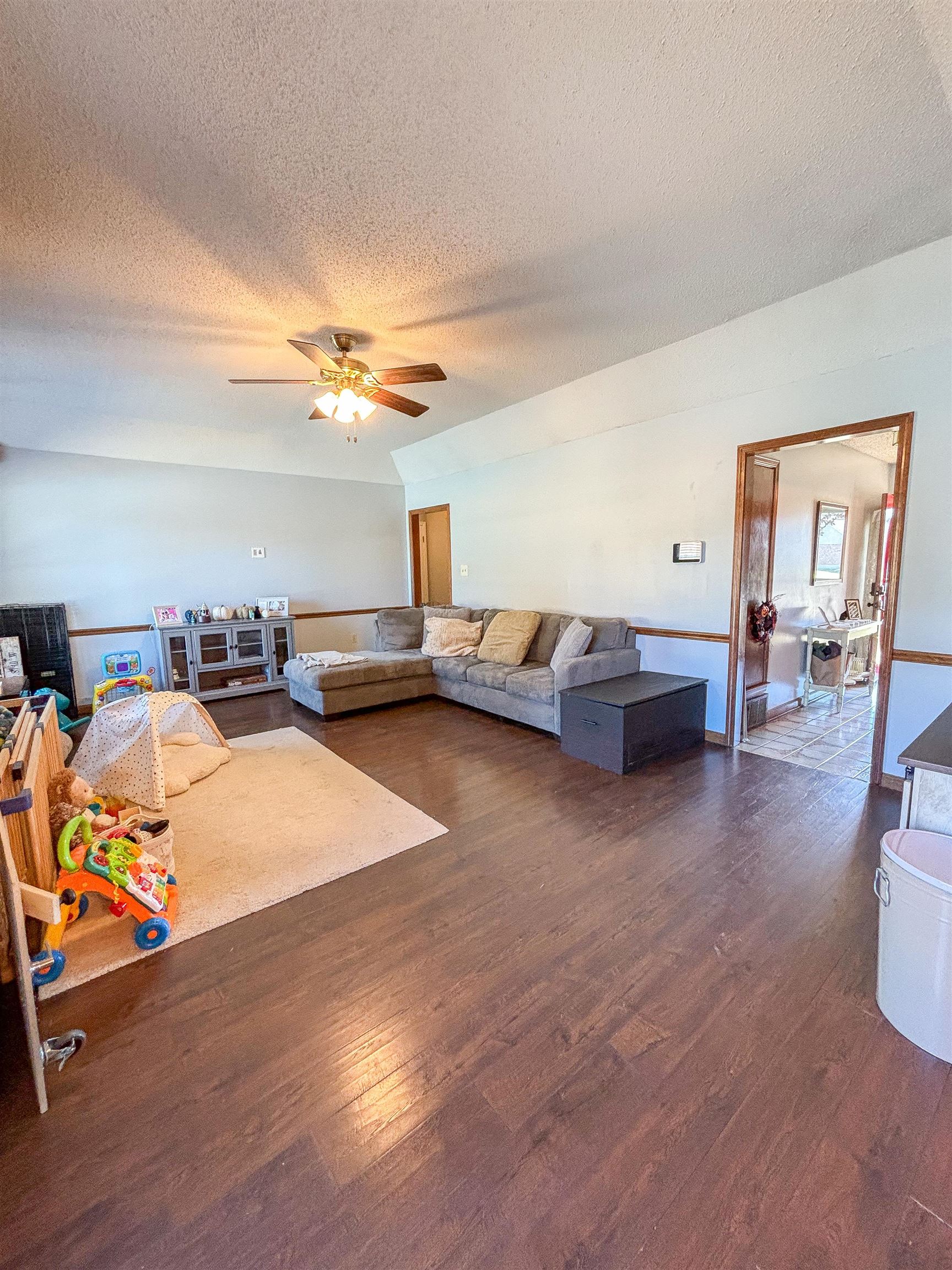 Living room with ceiling fan, a textured ceiling, and dark hardwood / wood-style floors