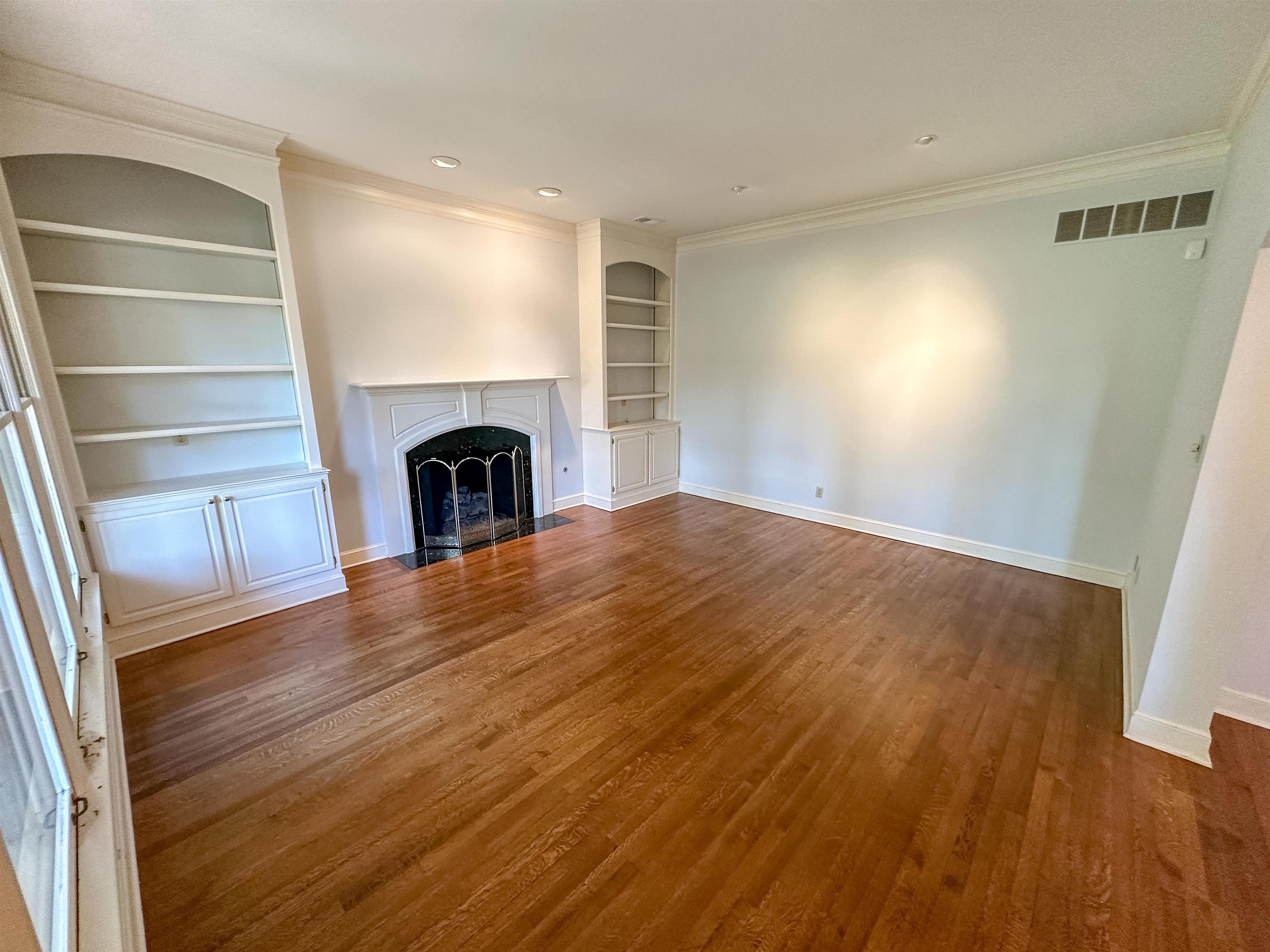 Unfurnished living room featuring dark wood-type flooring, crown molding, and built in shelves