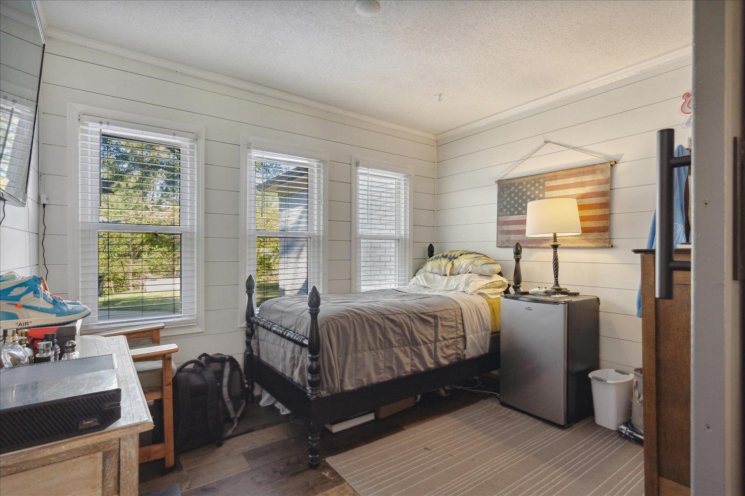 Bedroom with fridge, wooden walls, wood-type flooring, and a textured ceiling