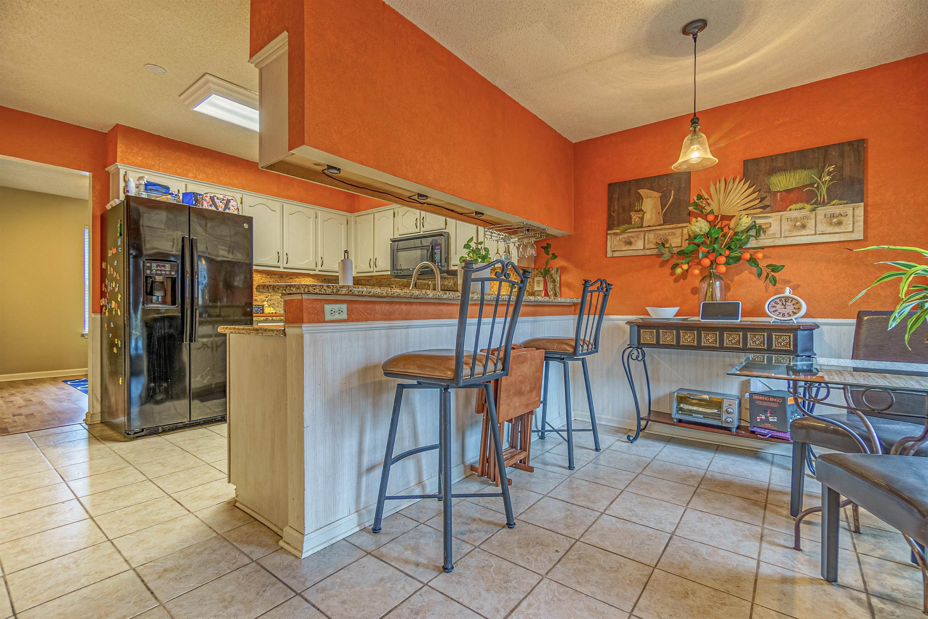 Kitchen with hanging light fixtures, kitchen peninsula, black fridge, a breakfast bar area, and a textured ceiling