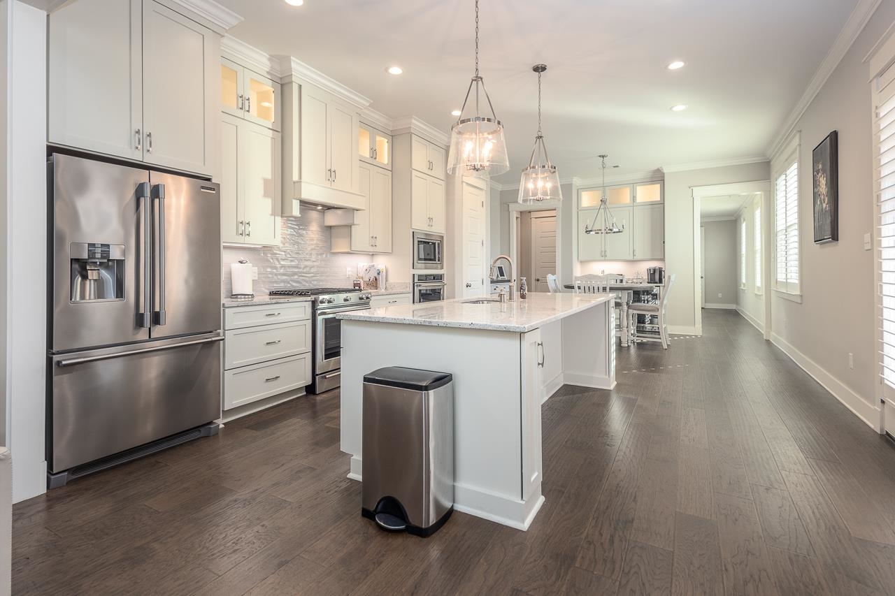 Kitchen with light stone counters, an island with sink, appliances with stainless steel finishes, dark wood-type flooring, and decorative light fixtures