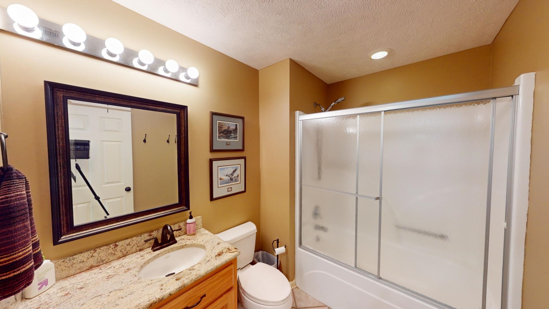 Full bathroom with toilet, a textured ceiling, vanity, and shower / bath combination with glass door