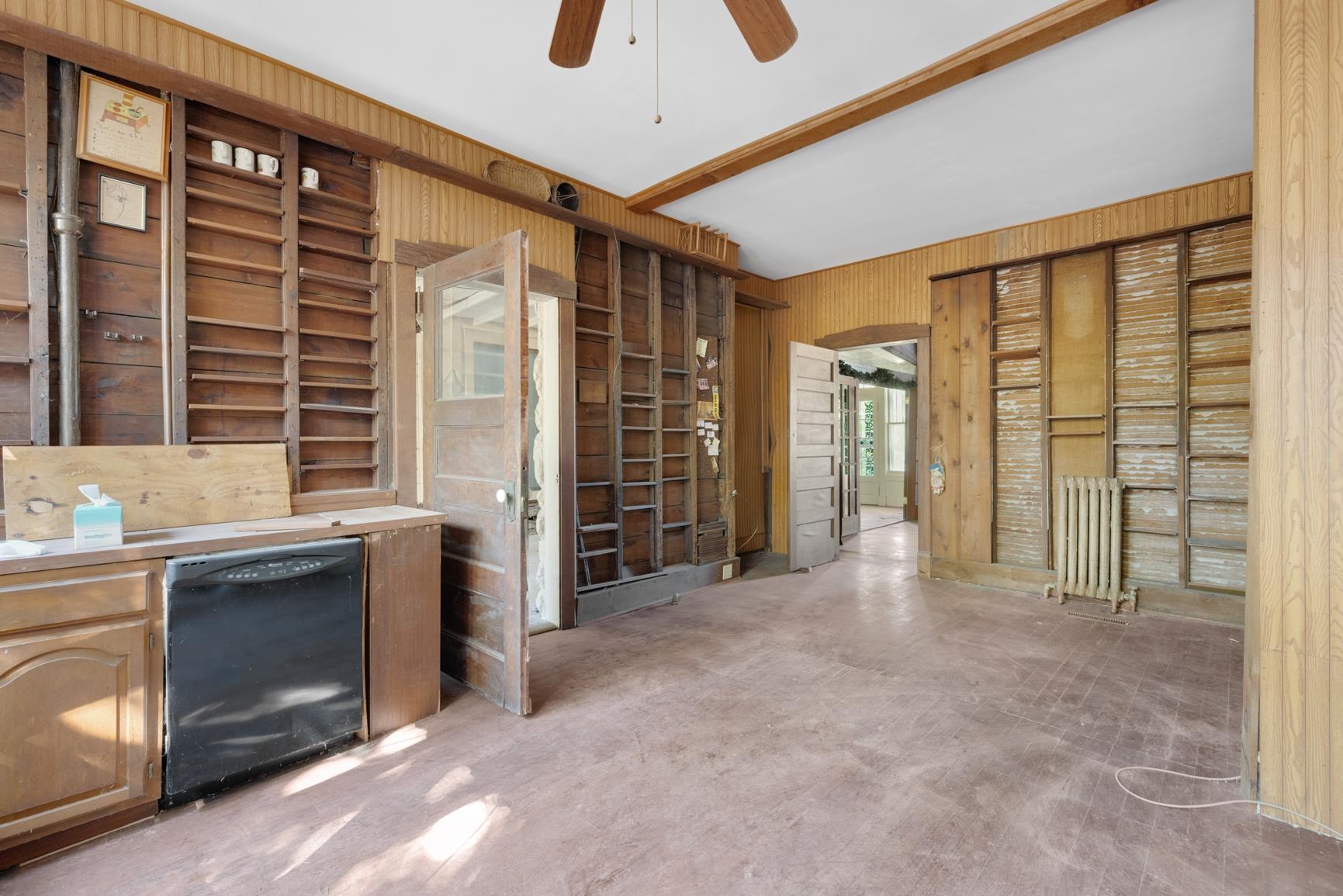 Interior space featuring ceiling fan, radiator heating unit, wooden walls, and black dishwasher