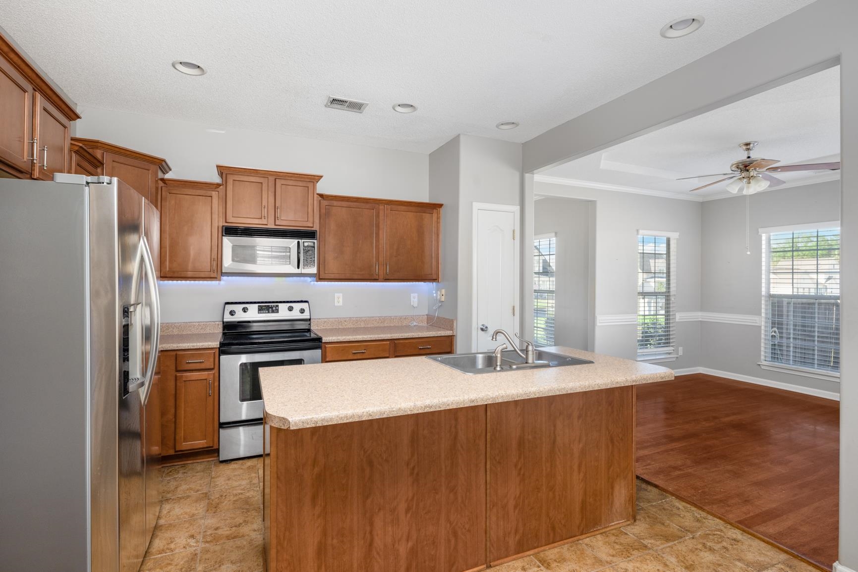 Kitchen with ceiling fan, a kitchen island with sink, light wood-type flooring, sink, and stainless steel appliances