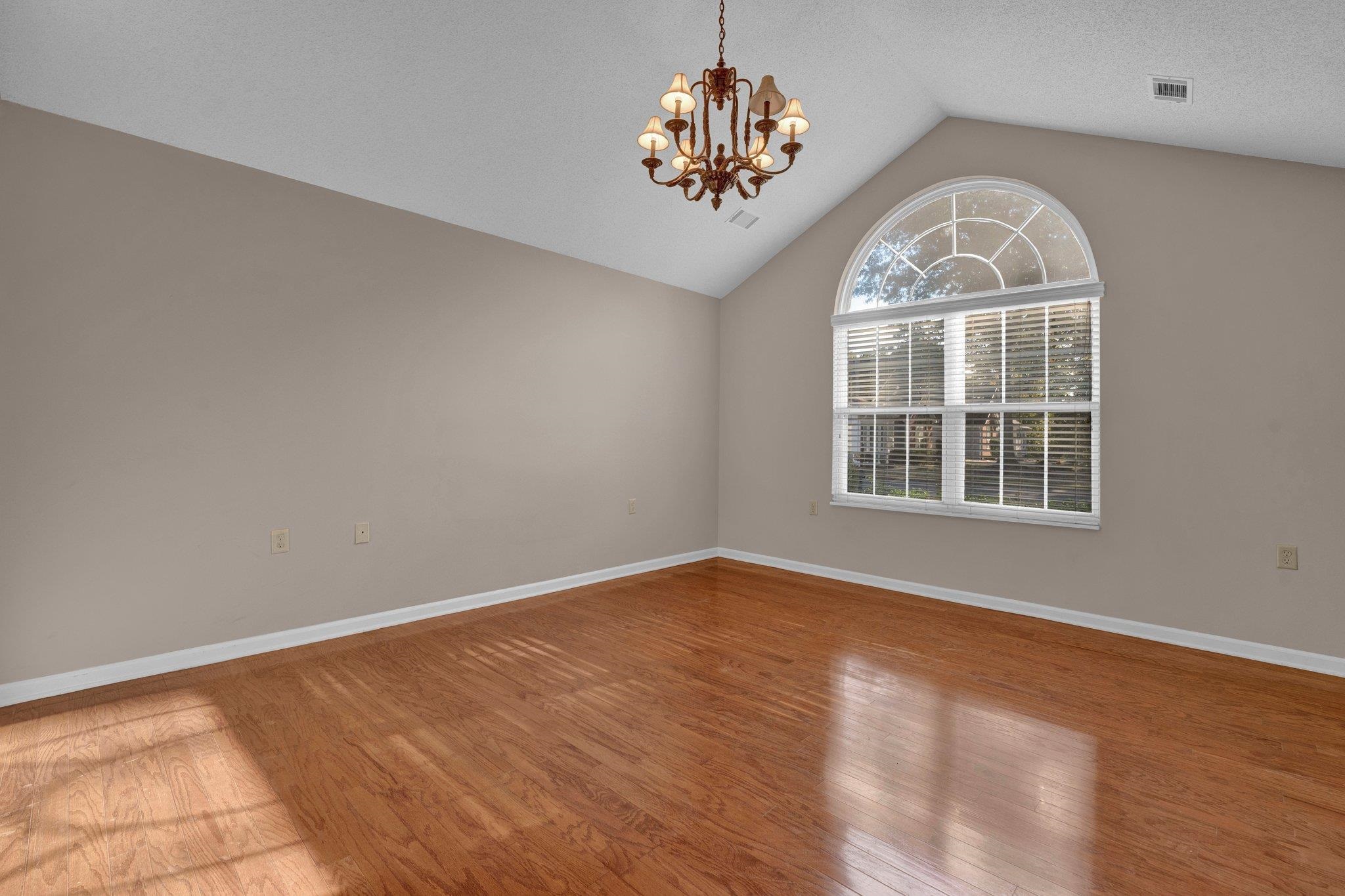 Empty room with lofted ceiling, hardwood / wood-style floors, a textured ceiling, and a notable chandelier