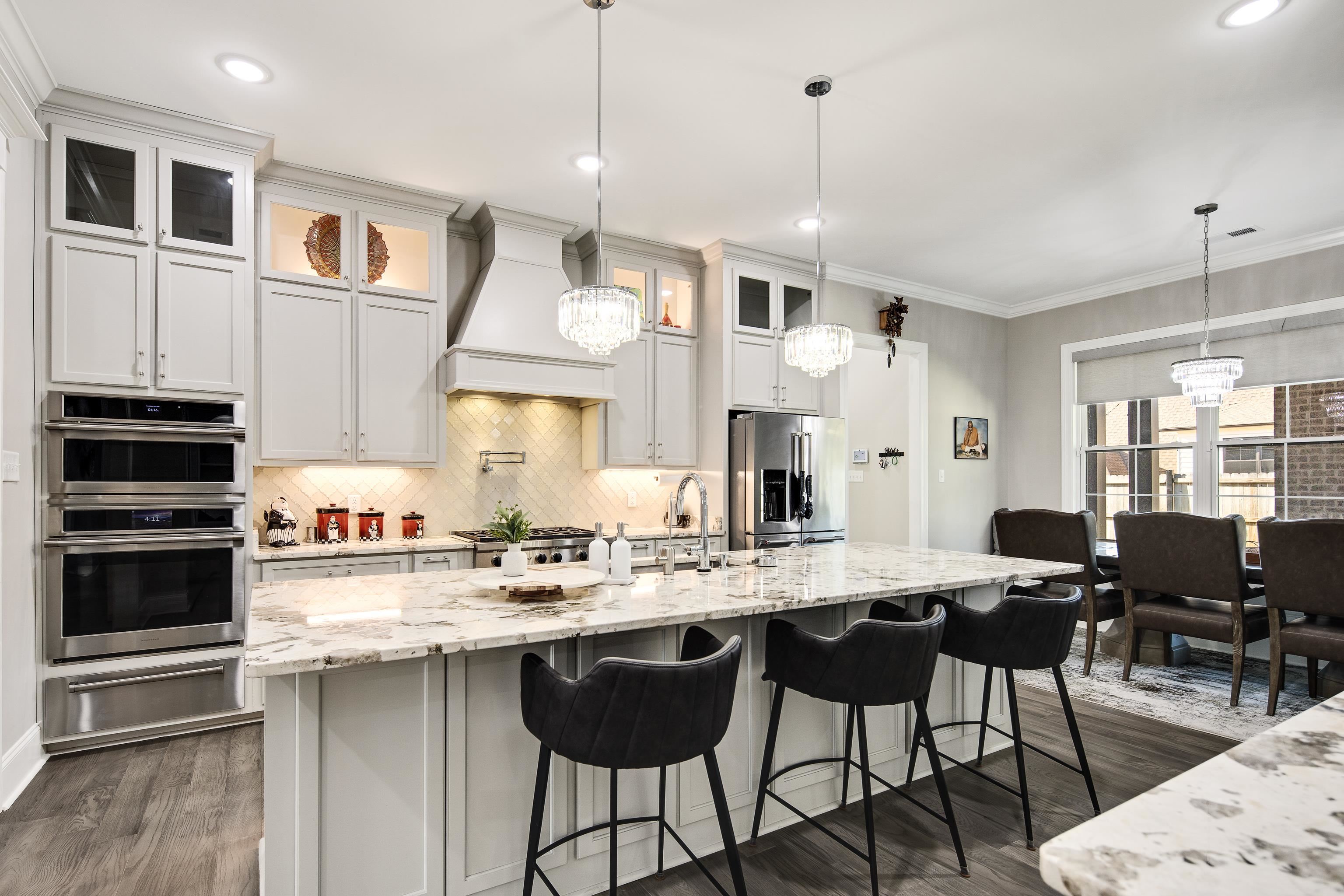 Kitchen with white cabinets, custom range hood, stainless steel appliances, and an island with sink