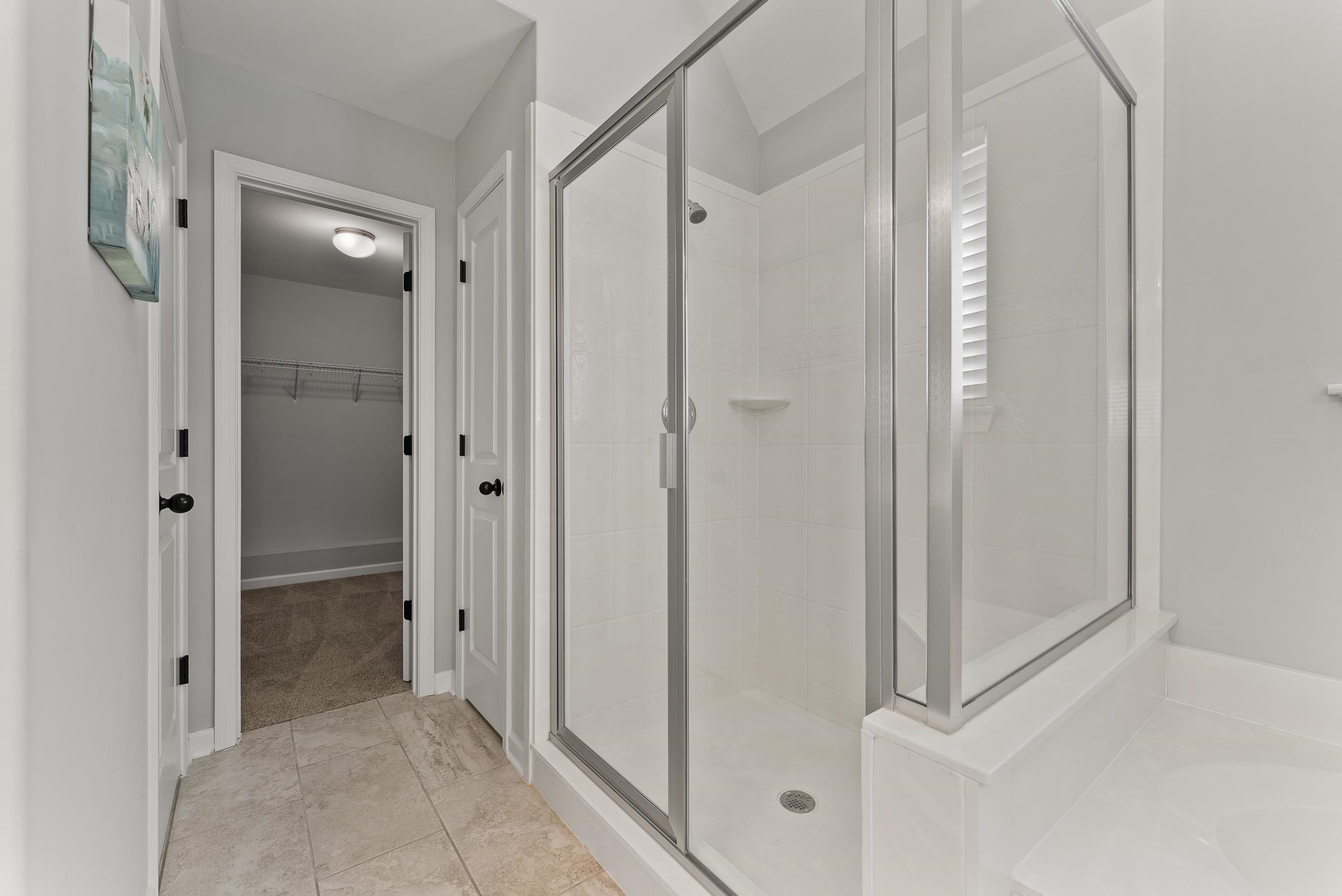 Bathroom featuring walk in shower, vaulted ceiling and tile patterned flooring with plenty of natural light. Large walk-in closet