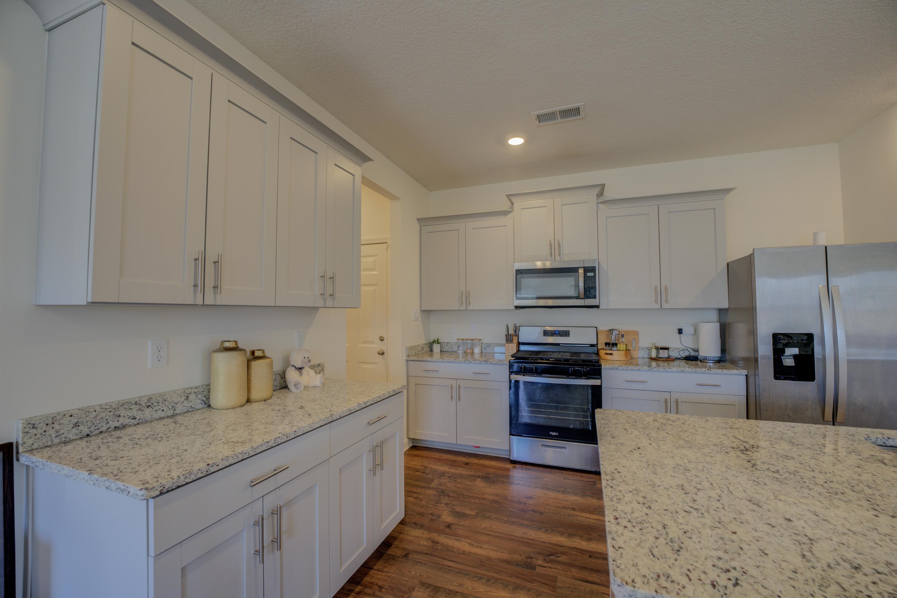 Kitchen with white cabinets, light stone counters, stainless steel appliances, and dark hardwood / wood-style flooring