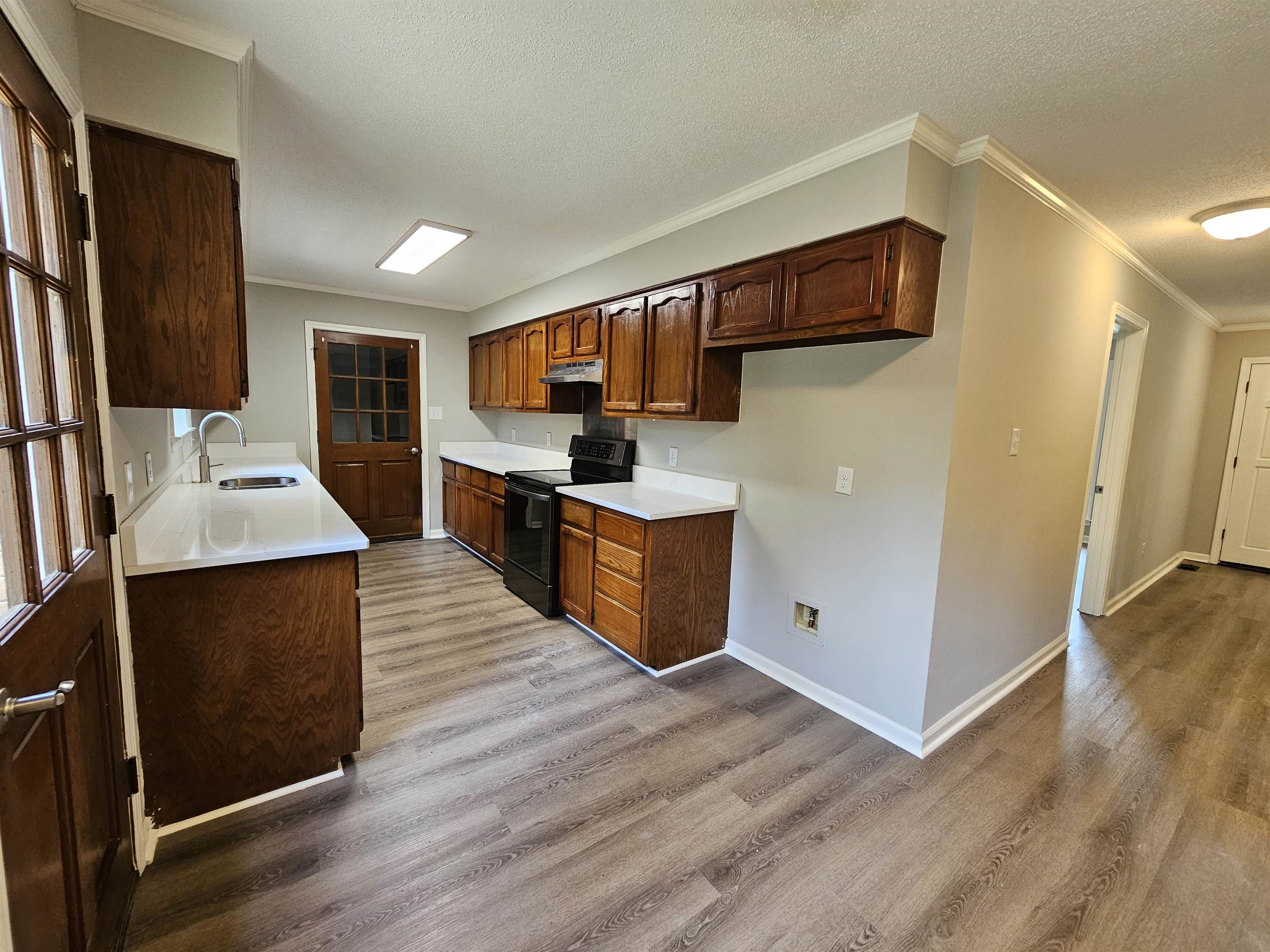 Kitchen featuring a textured ceiling, light wood-type flooring, black electric range, crown molding, and sink