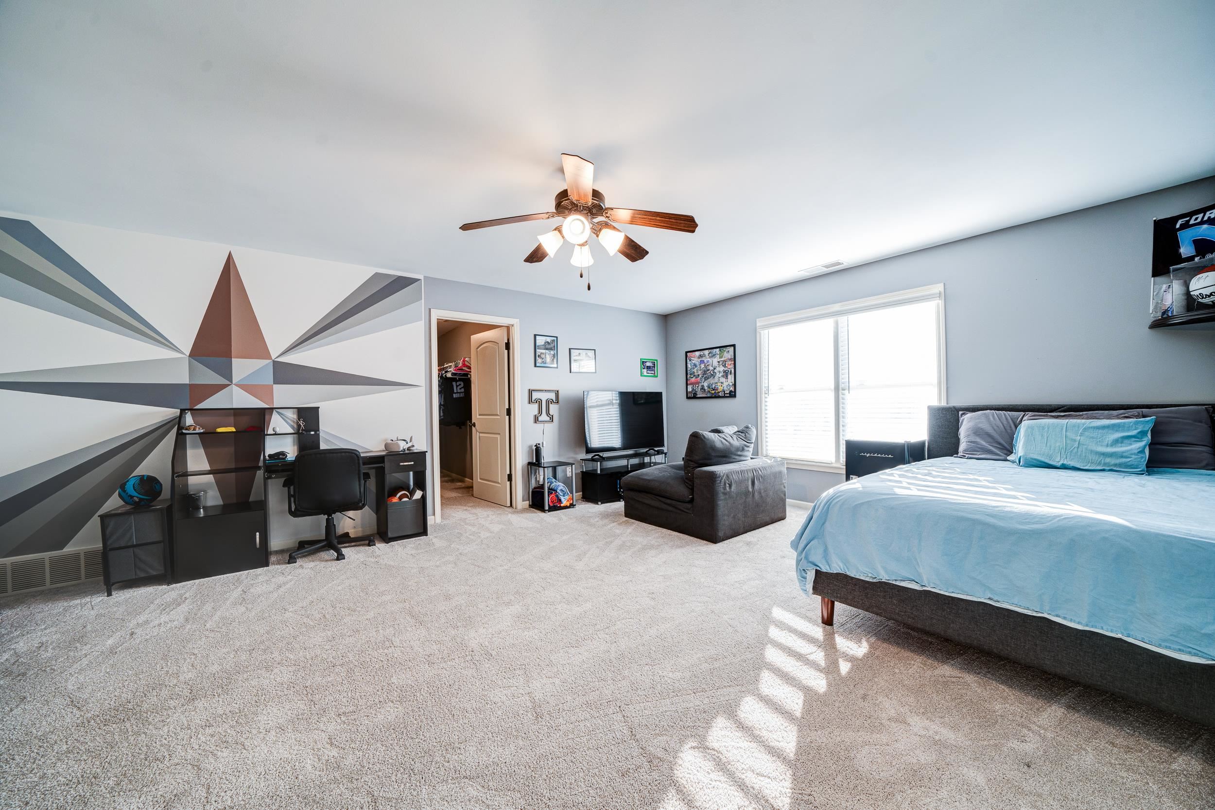 Carpeted bedroom with a spacious closet and ceiling fan