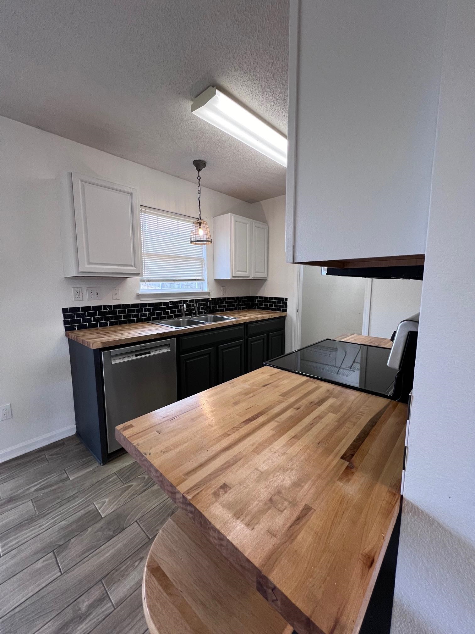 Kitchen featuring stainless steel dishwasher, white cabinetry, sink, wood counters,.