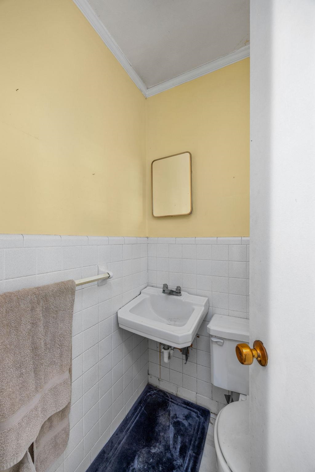 Bathroom featuring toilet, tile patterned flooring, crown molding, sink, and tile walls