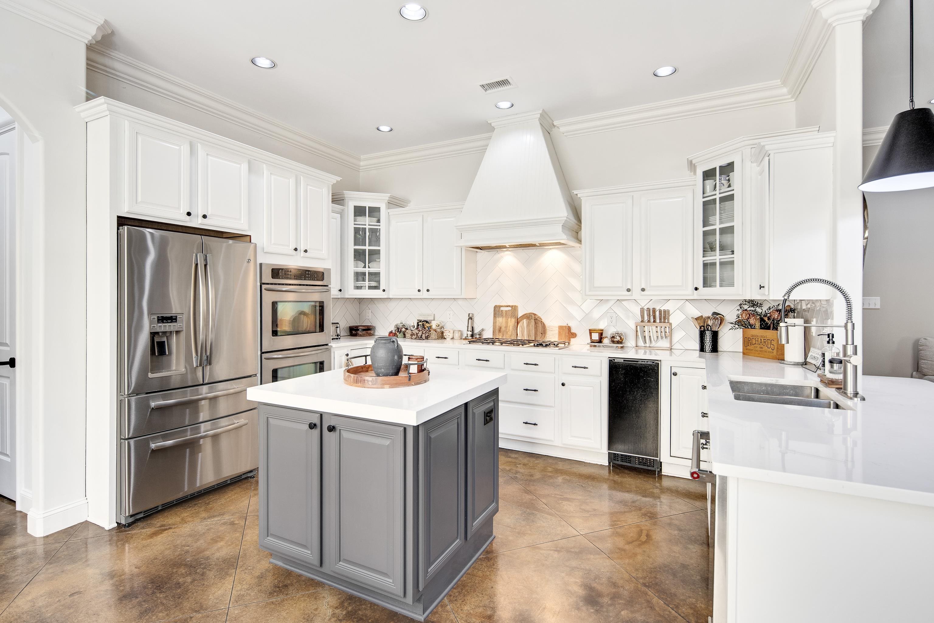 Kitchen with appliances with stainless steel finishes, white cabinetry, custom range hood, and sink