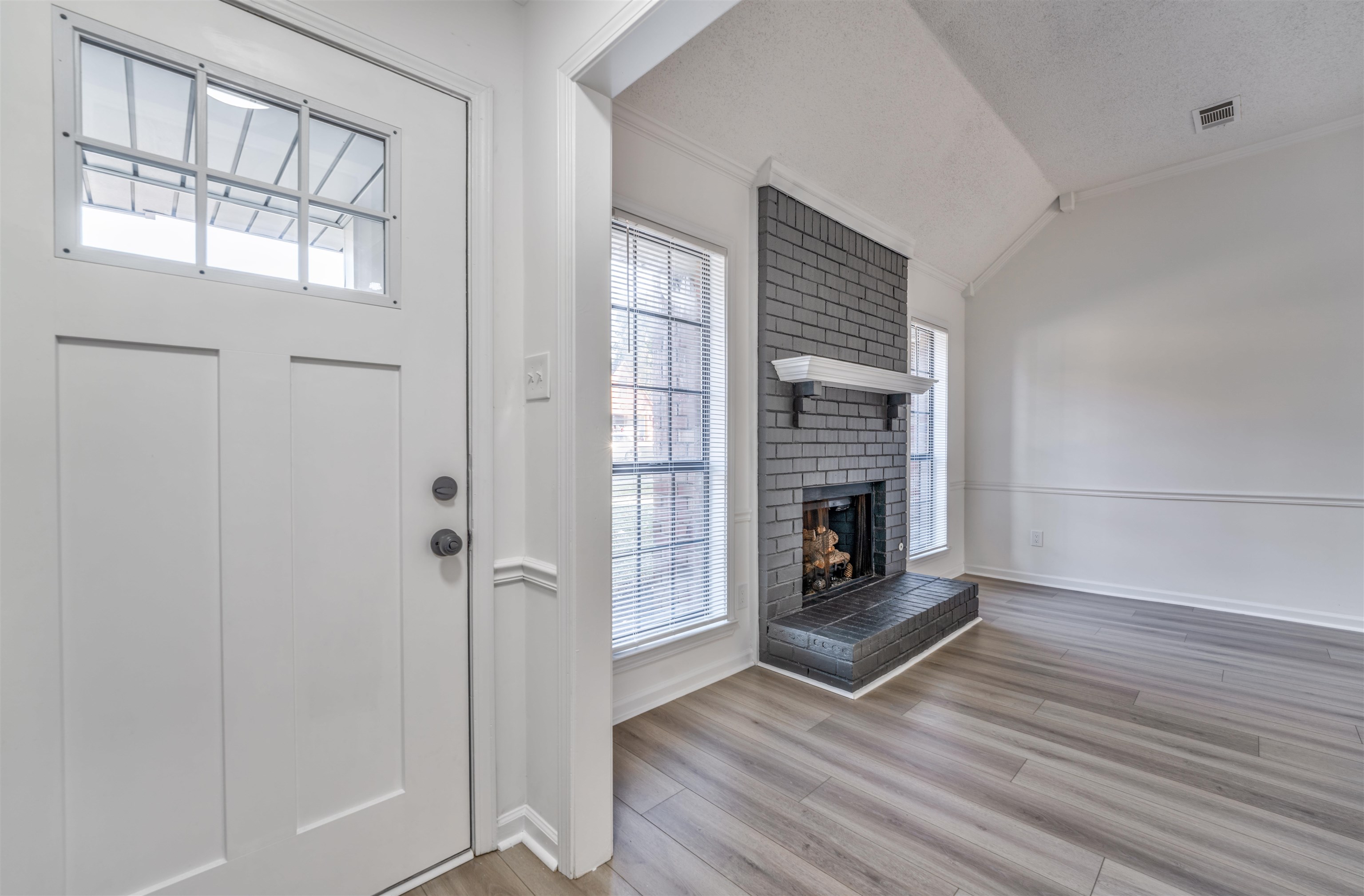 Foyer entrance with a fireplace, crown molding, vaulted ceiling, a textured ceiling, and light hardwood / wood-style floors