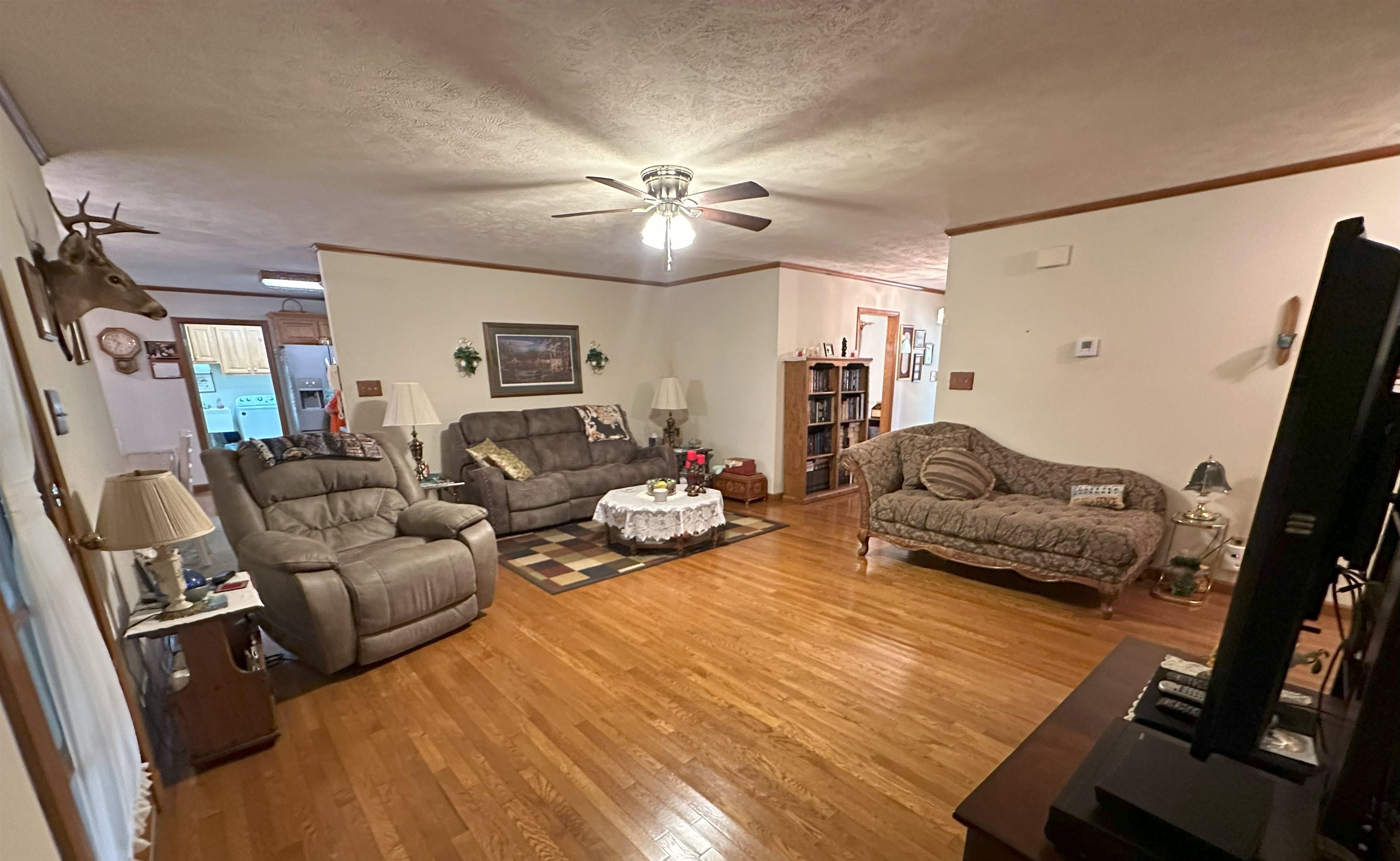 Living room featuring hardwood / wood-style floors, crown molding, a textured ceiling, and ceiling fan