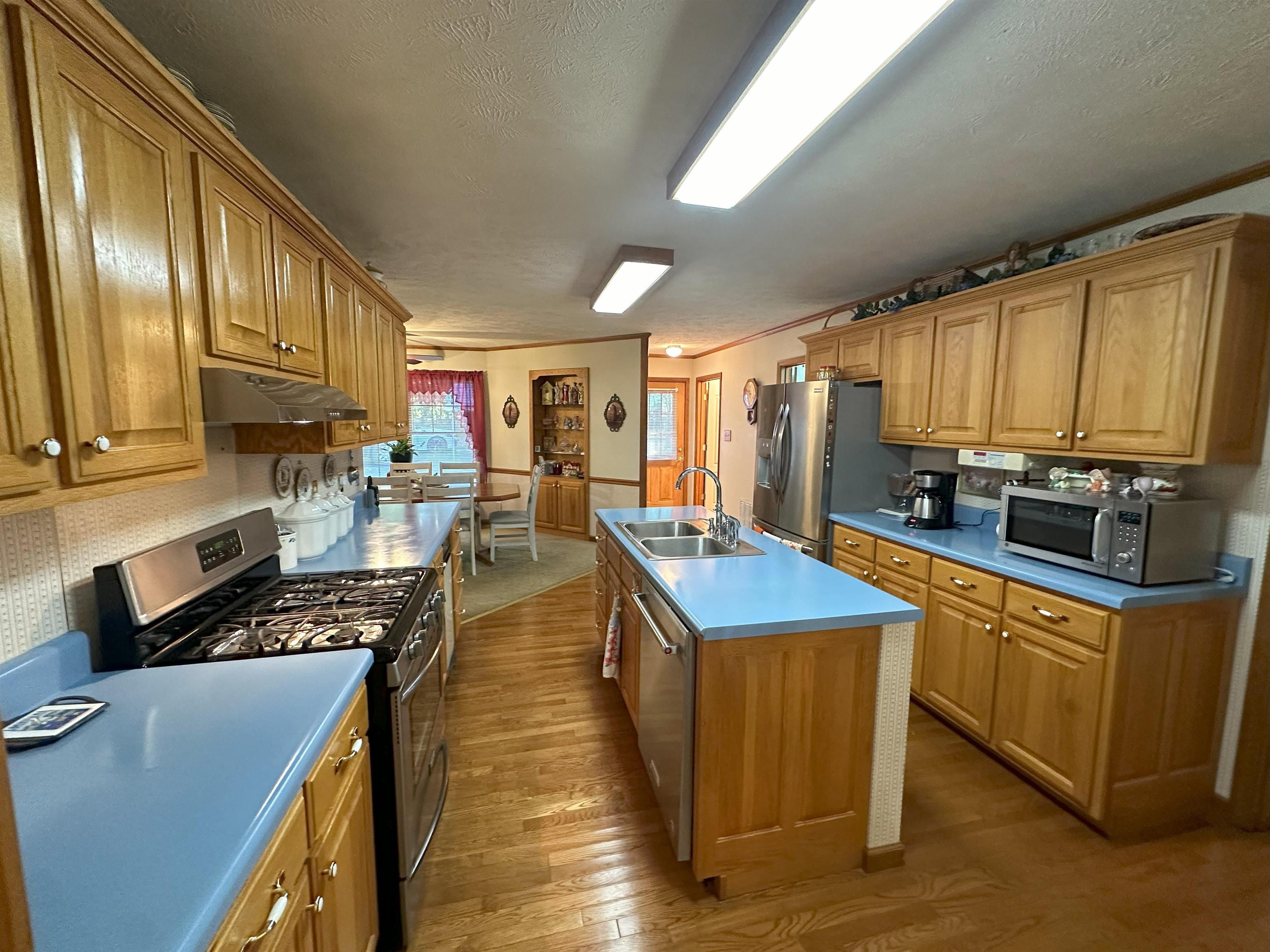Kitchen featuring a textured ceiling, a kitchen island with sink, light hardwood / wood-style flooring, sink, and stainless steel appliances