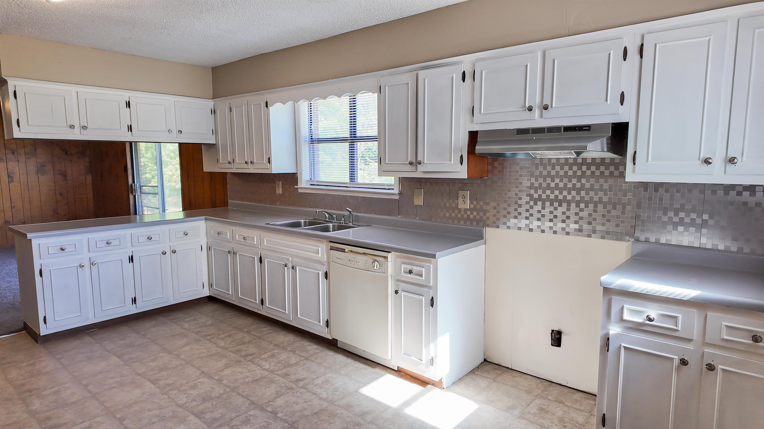 Kitchen with white cabinets, tasteful backsplash, exhaust hood, white dishwasher, and sink