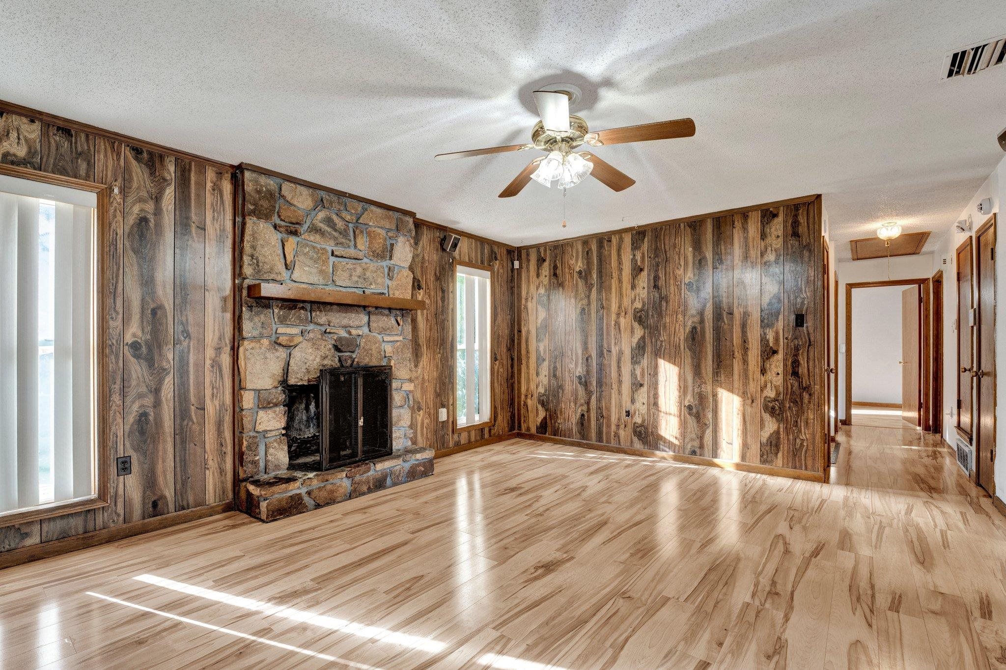 Unfurnished living room featuring light hardwood / wood-style flooring, a textured ceiling, and wooden walls