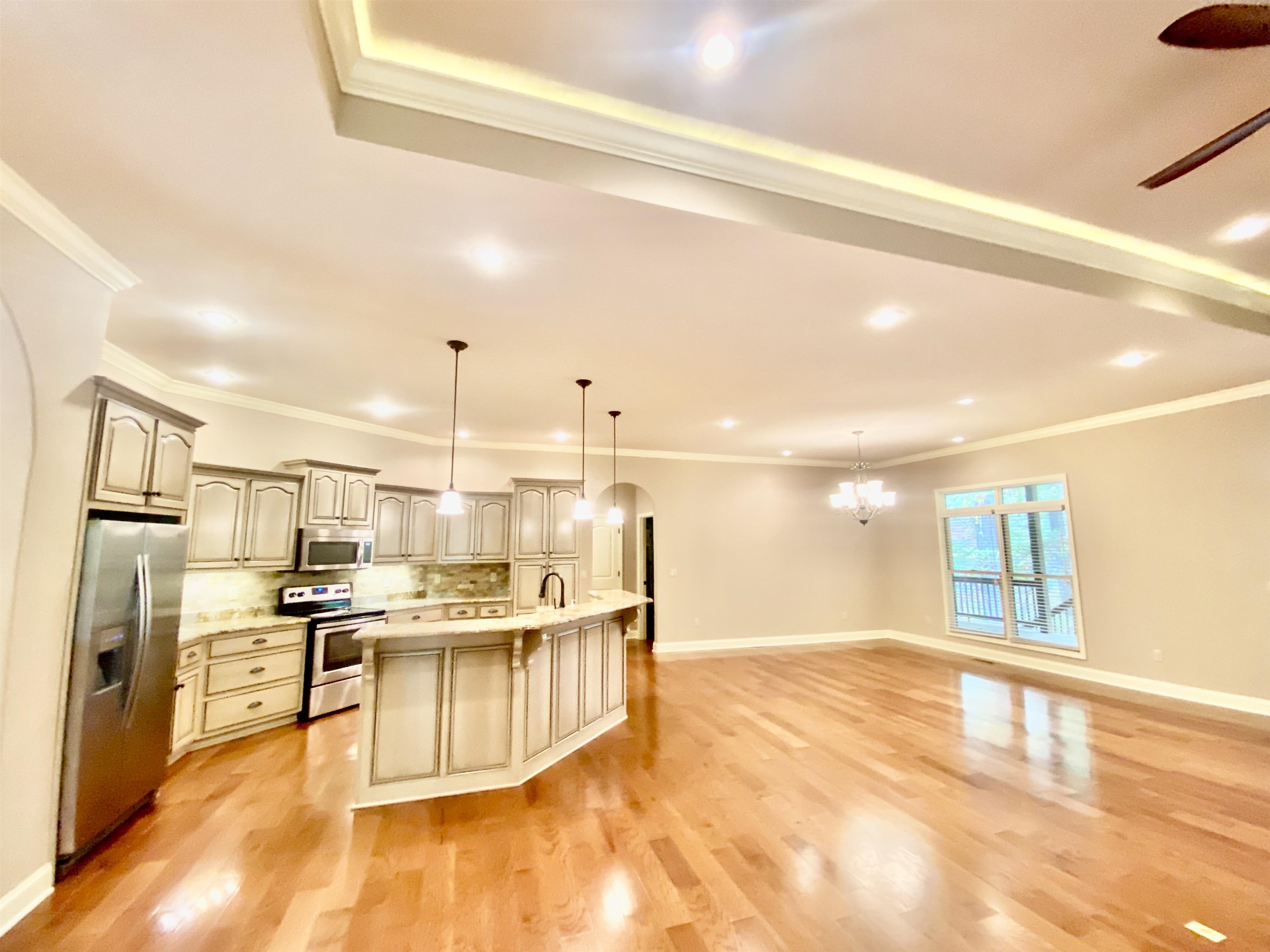 Kitchen featuring appliances with stainless steel finishes, an island with sink, hard wood flooring, and pendant lighting