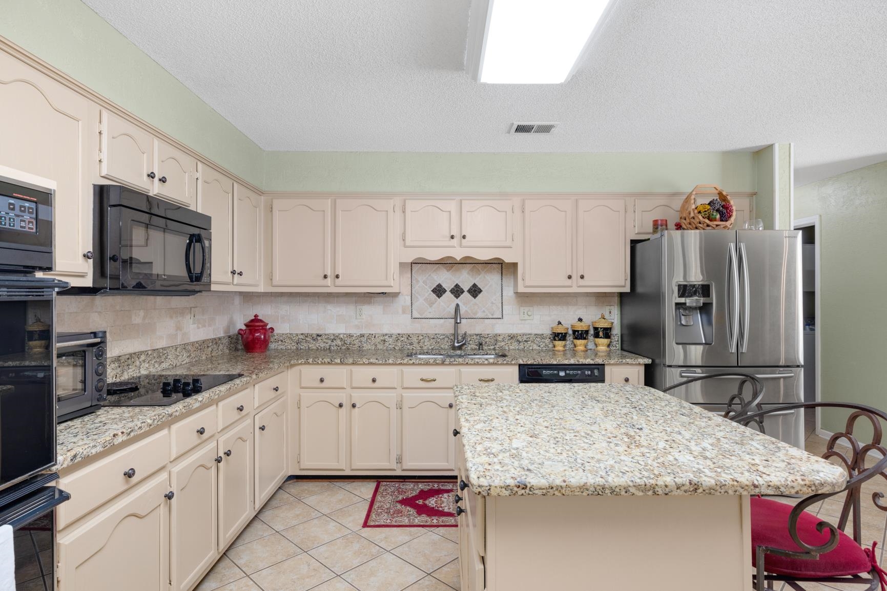 Kitchen with tasteful backsplash, a kitchen island, light stone countertops, black appliances, and sink