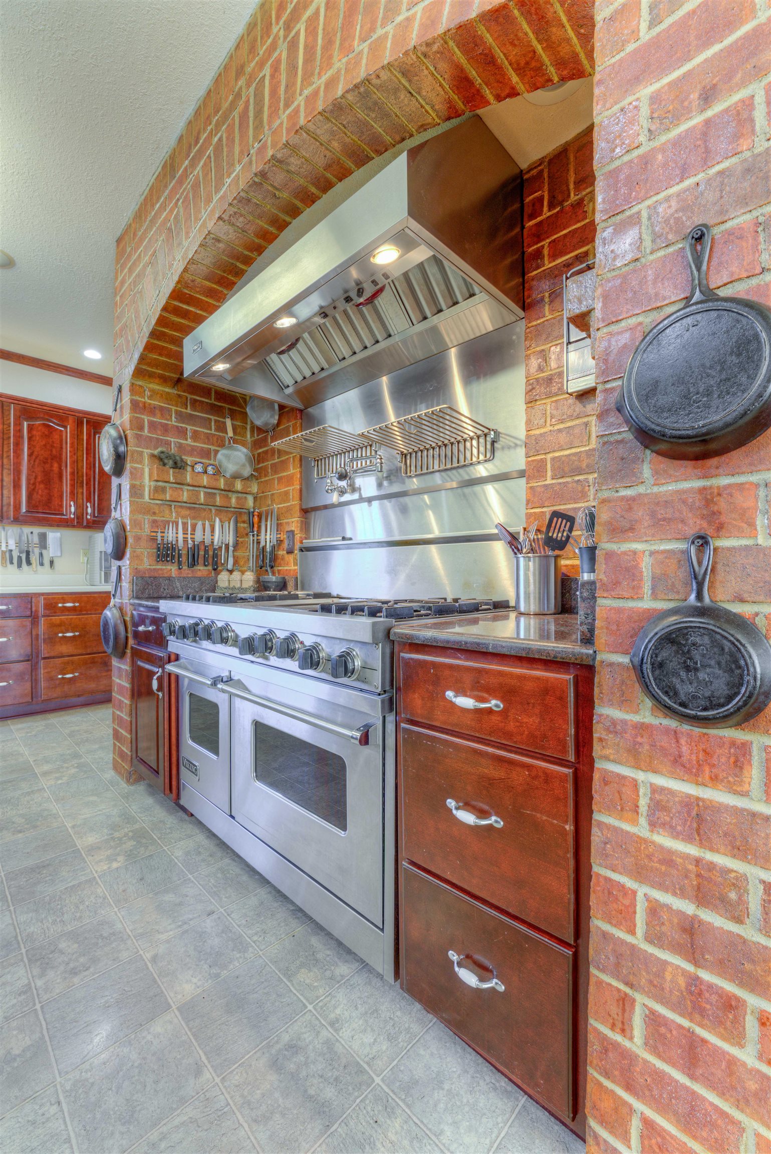 Kitchen featuring wall chimney exhaust hood, brick wall, range with two ovens, and backsplash