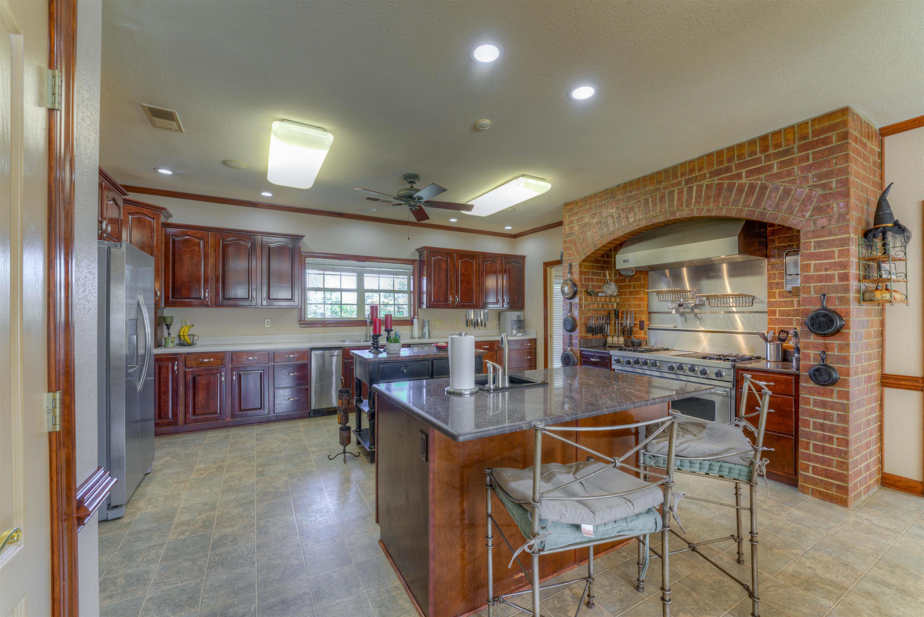 Kitchen with a kitchen island with sink, wall chimney range hood, a breakfast bar, appliances with stainless steel finishes, and ceiling fan