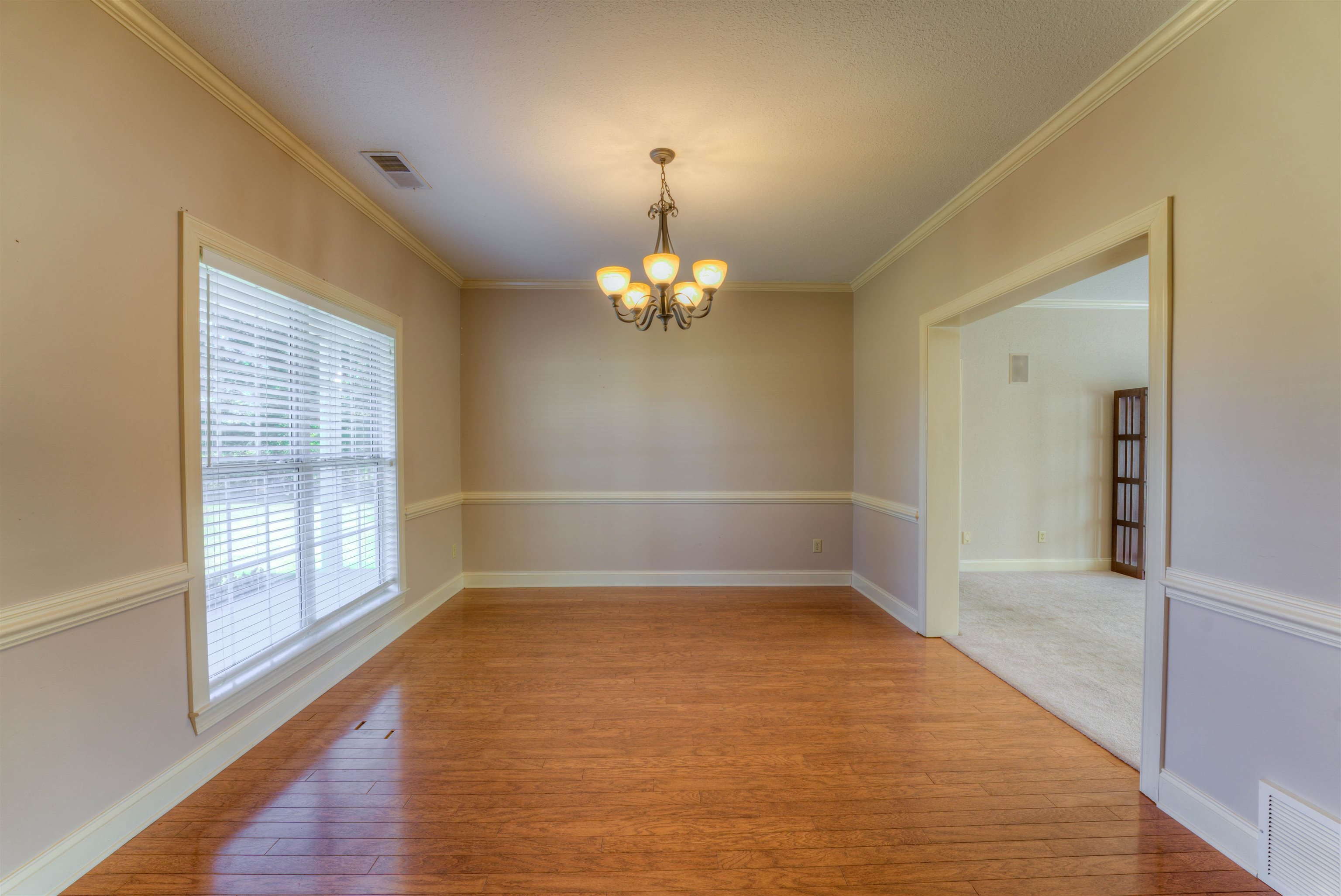 Empty room featuring an inviting chandelier, light wood-type flooring, and crown molding