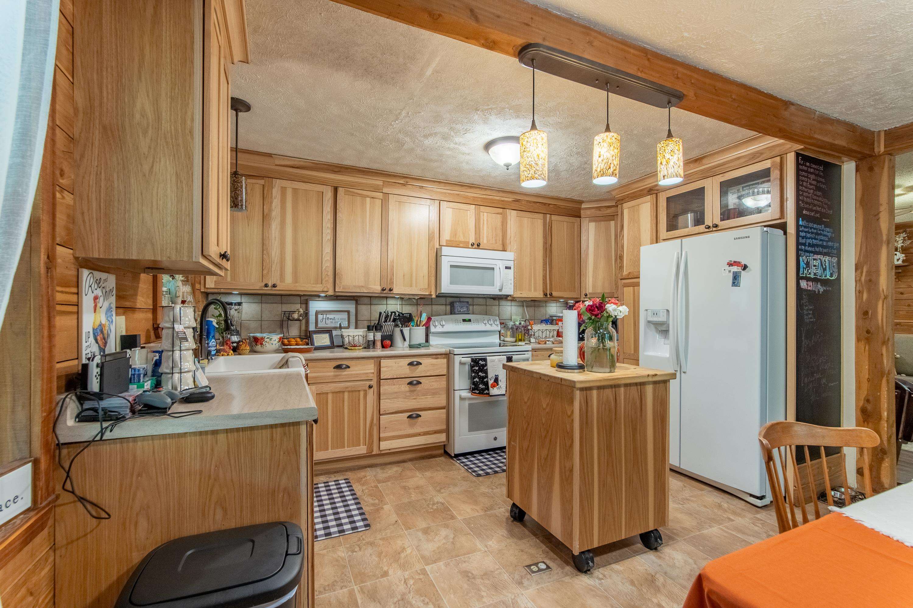 Kitchen with a textured ceiling, a center island, sink, and white appliances