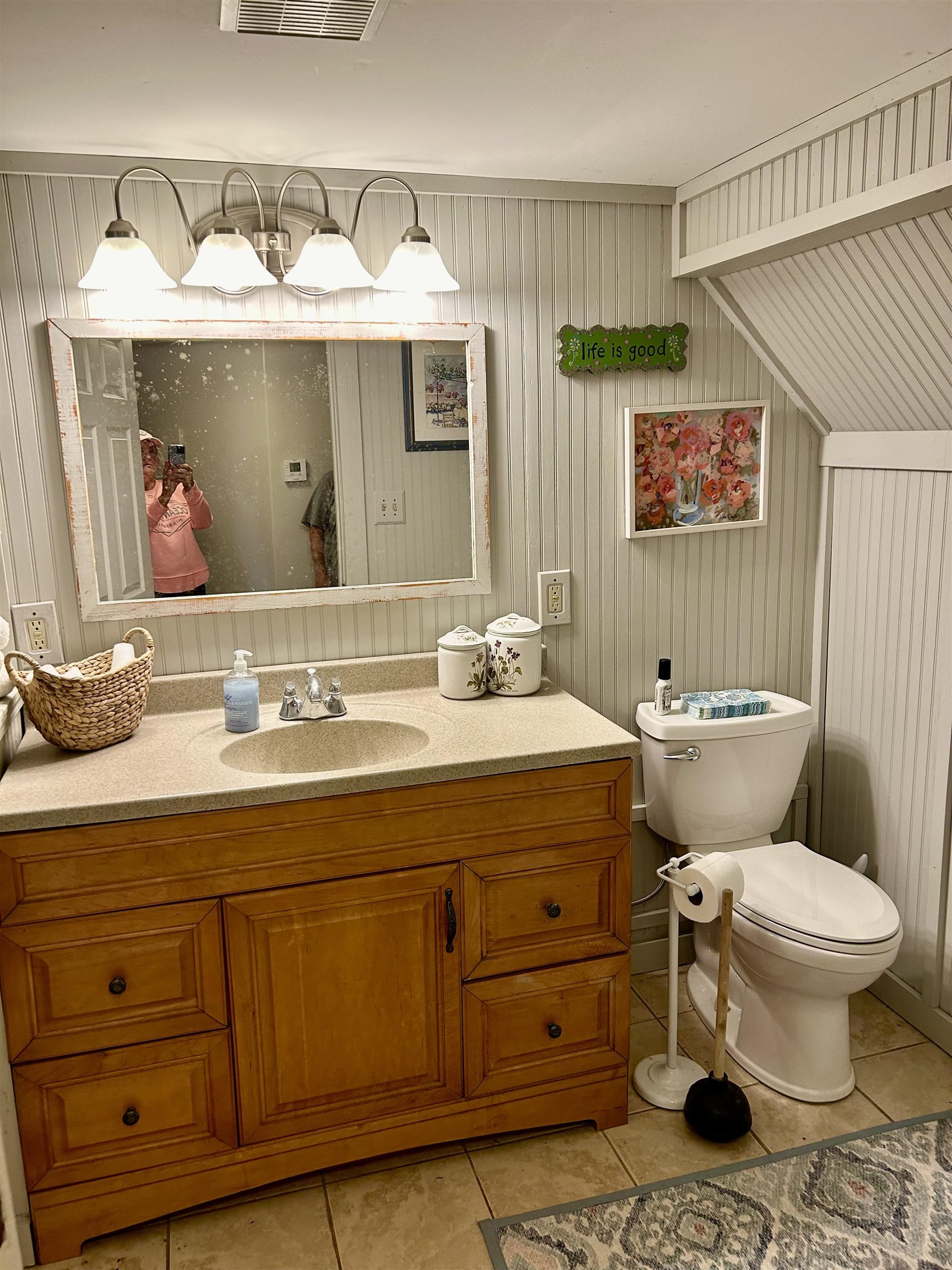 Bathroom with lofted ceiling, toilet, wood walls, vanity, and tile patterned flooring located in partial basement