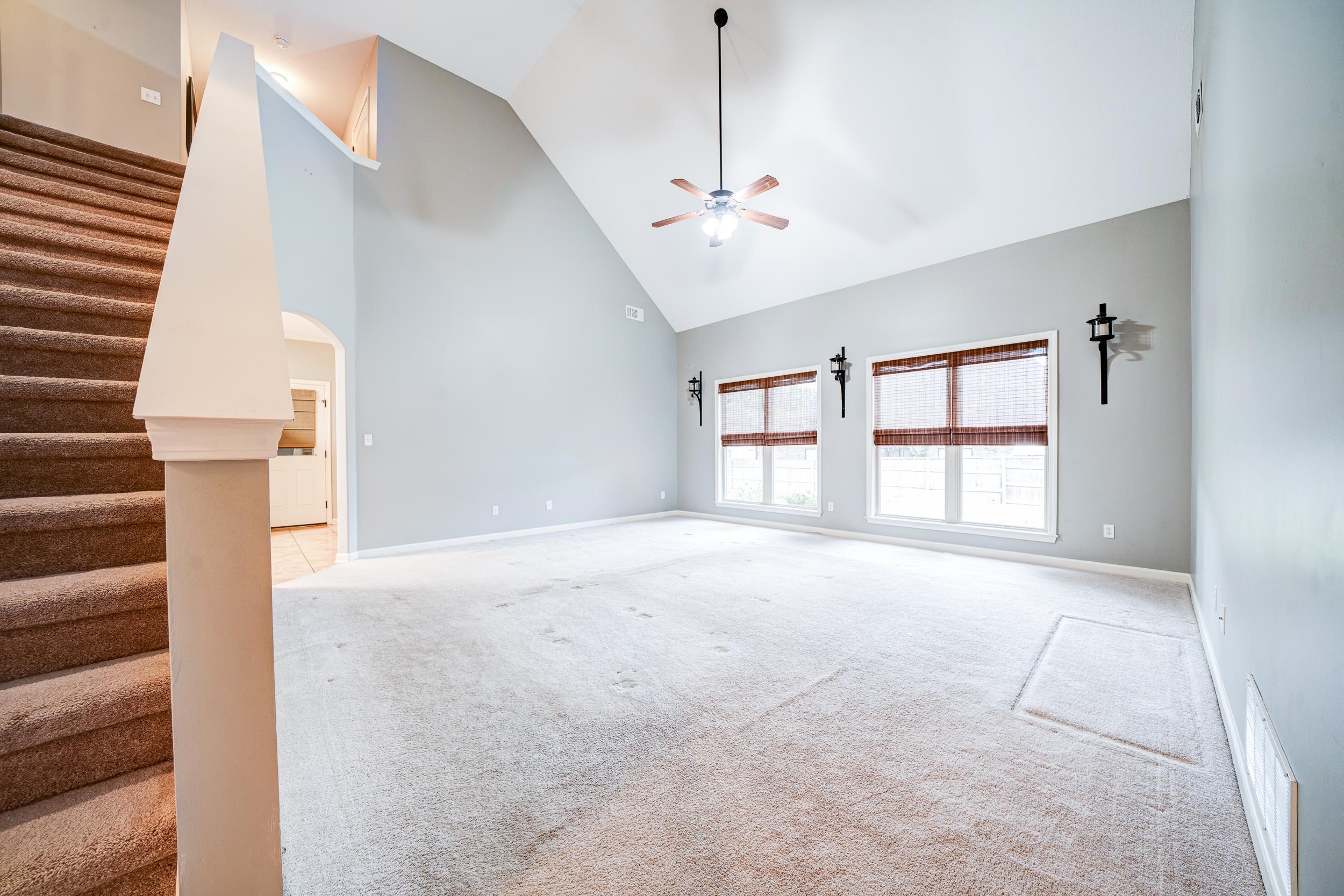 Unfurnished living room with light colored carpet, high vaulted ceiling, and ceiling fan