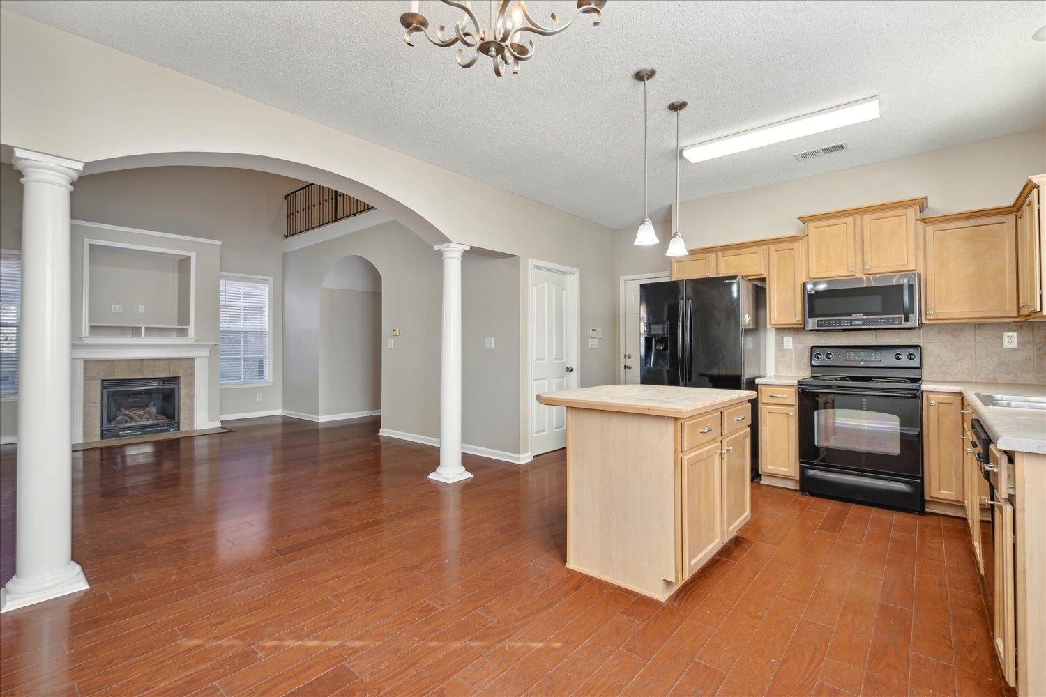 Kitchen featuring wood-type flooring, black appliances, a center island, decorative light fixtures, and a textured ceiling