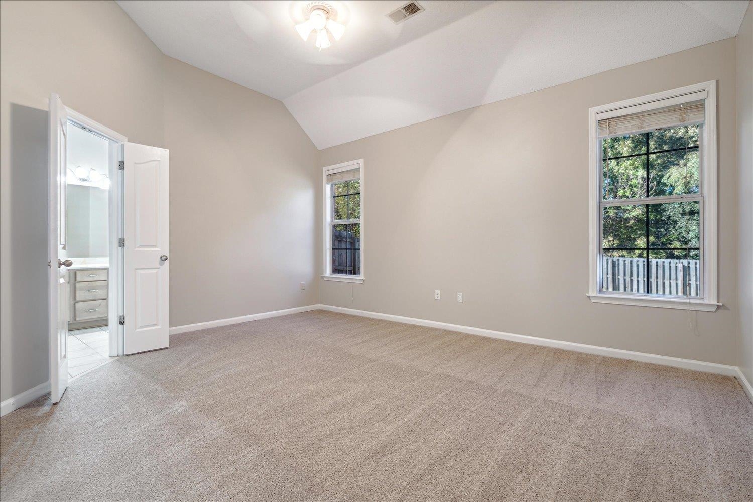 Spare room with a wealth of natural light, vaulted ceiling, and light carpet