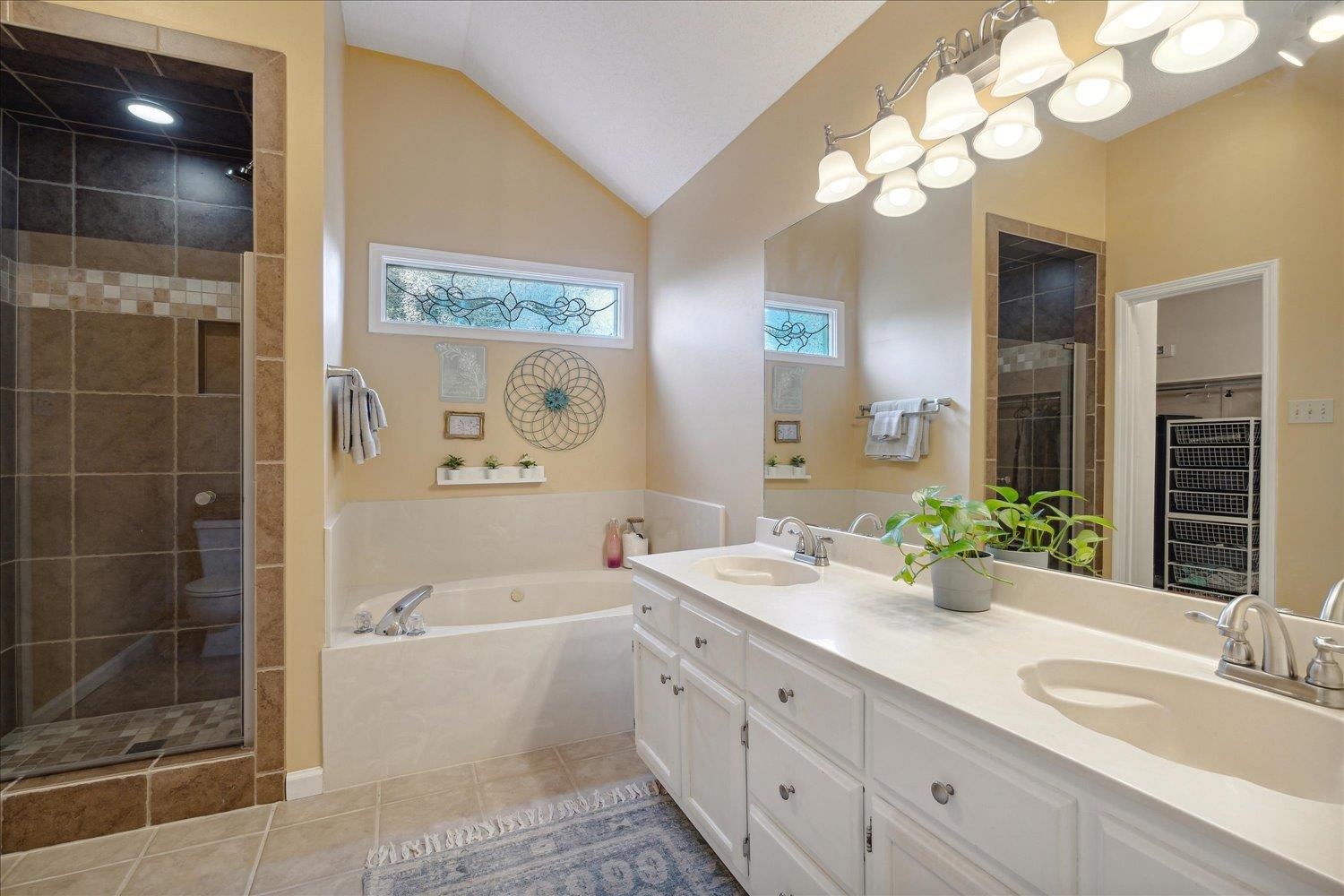 Bathroom featuring vanity, plus walk in shower, lofted ceiling, and tile patterned flooring