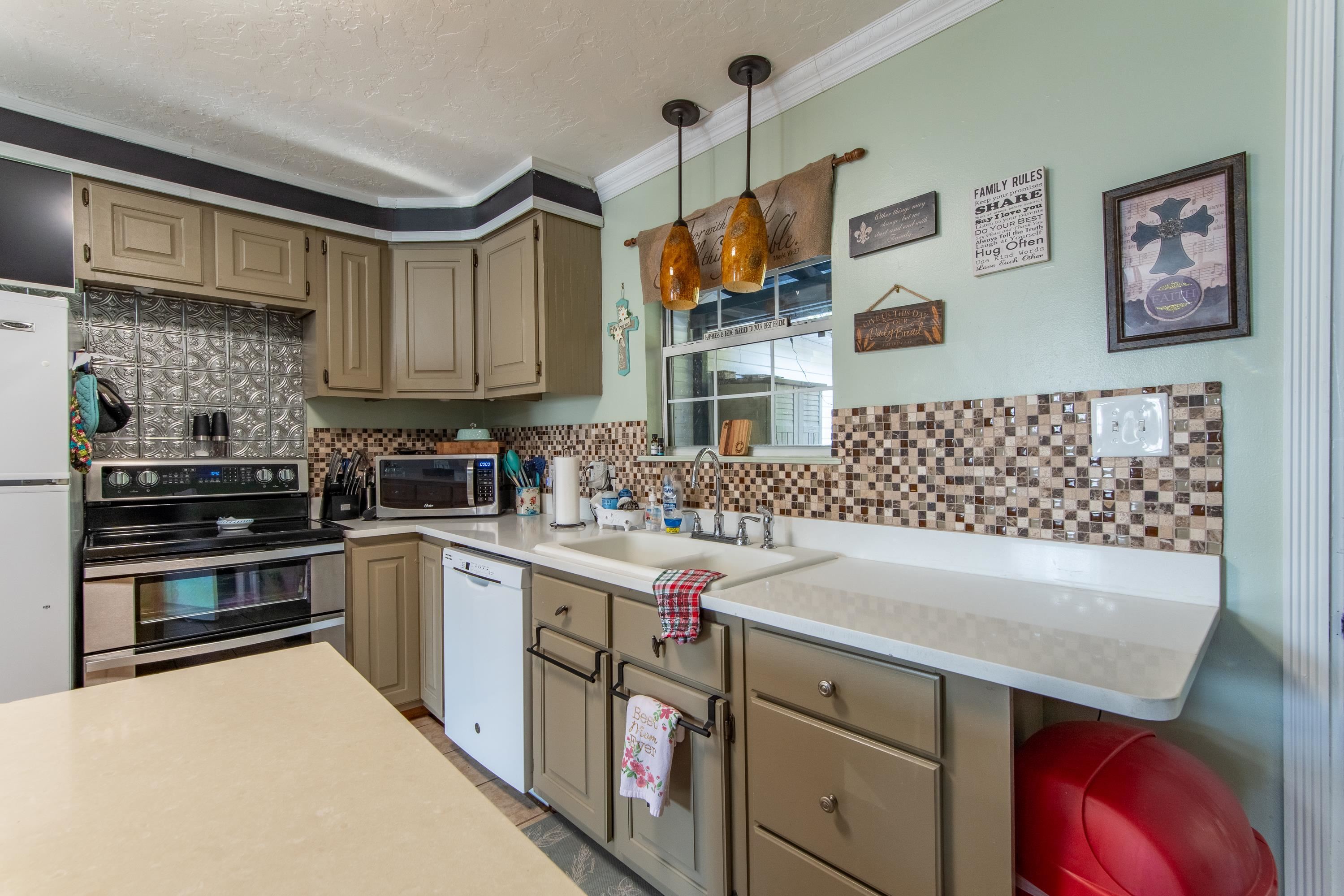 Kitchen featuring ornamental molding, decorative light fixtures, stainless steel appliances, and tasteful backsplash