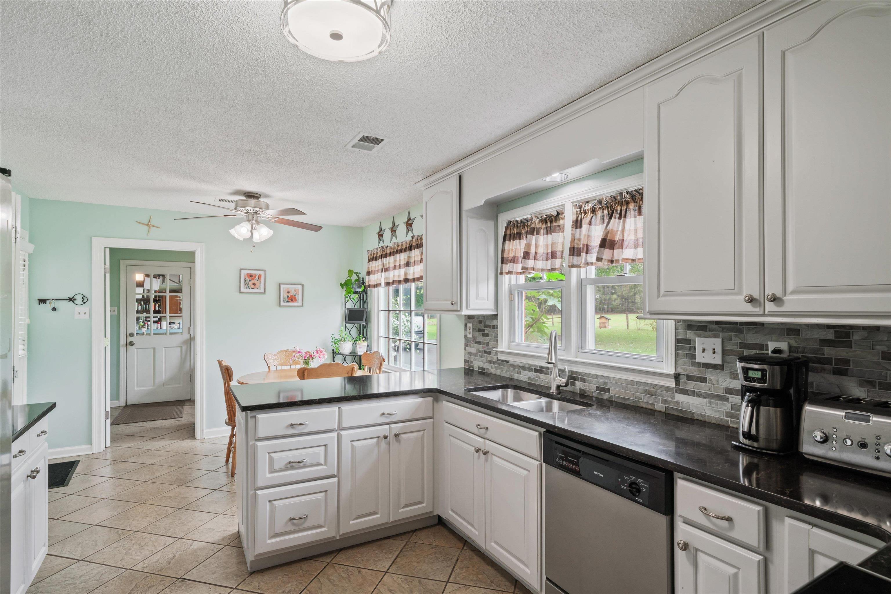 Kitchen with ceiling fan, white cabinetry, and stainless steel dishwasher