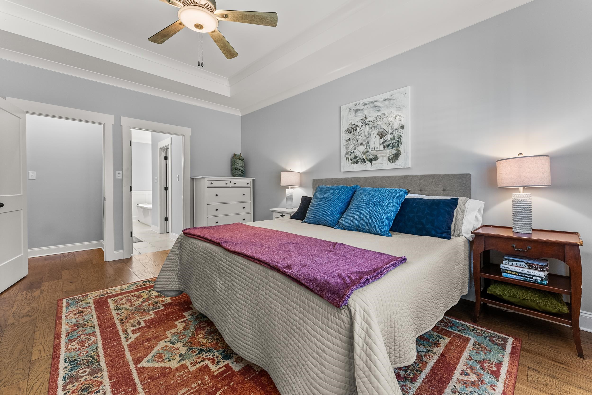 Bedroom with ensuite bath, a raised ceiling, hardwood / wood-style flooring, and ceiling fan