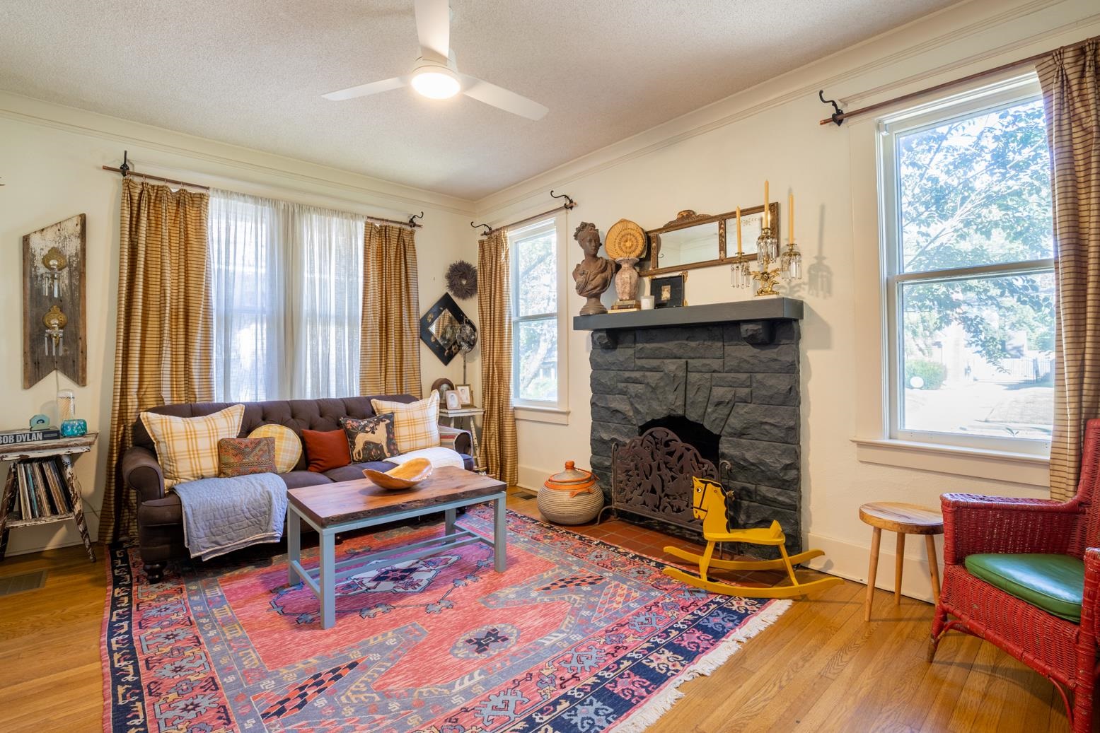 Living room with a stone fireplace, hardwood flooring, ornamental molding, a textured ceiling, and ceiling fan