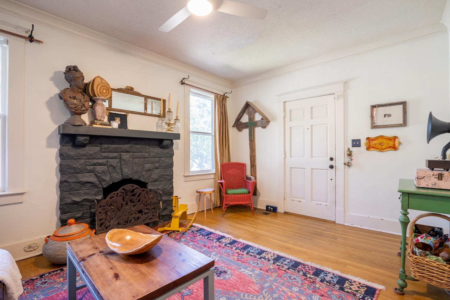 Living room featuring ceiling fan, crown molding, hardwood  flooring, and a stone fireplace