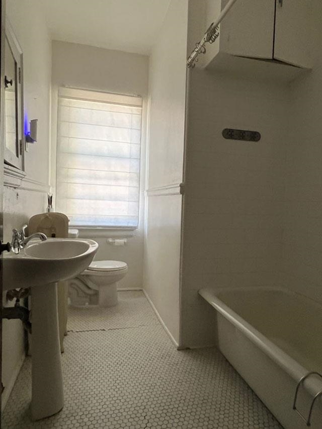 Bathroom with toilet, a washtub, and tile patterned flooring