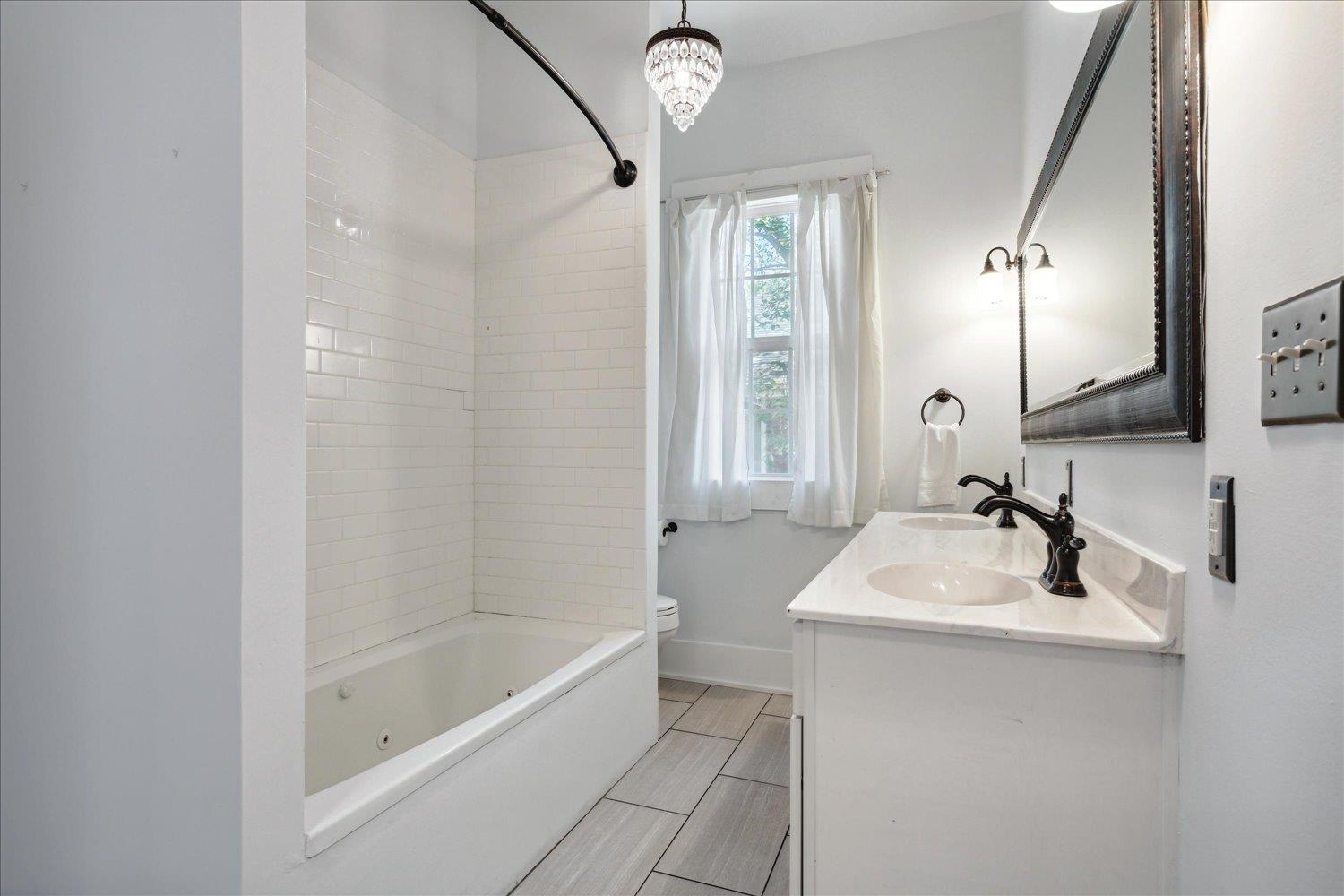 Full bathroom with toilet, a notable chandelier, tiled shower / bath combo, and vanity