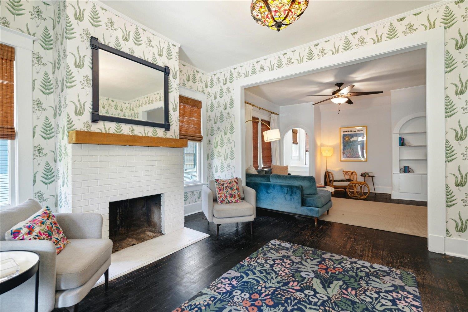 Living room featuring dark wood-type flooring, ceiling fan, built in features, and a brick fireplace