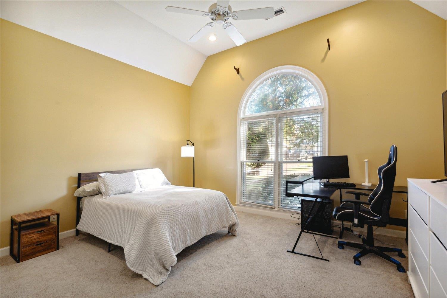 Bedroom featuring ceiling fan, light carpet, and vaulted ceiling