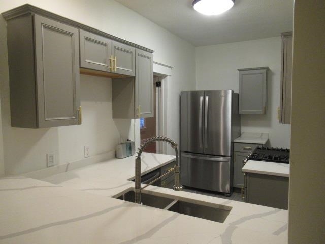 Kitchen featuring sink, stainless steel fridge, light stone countertops, and gray cabinetry