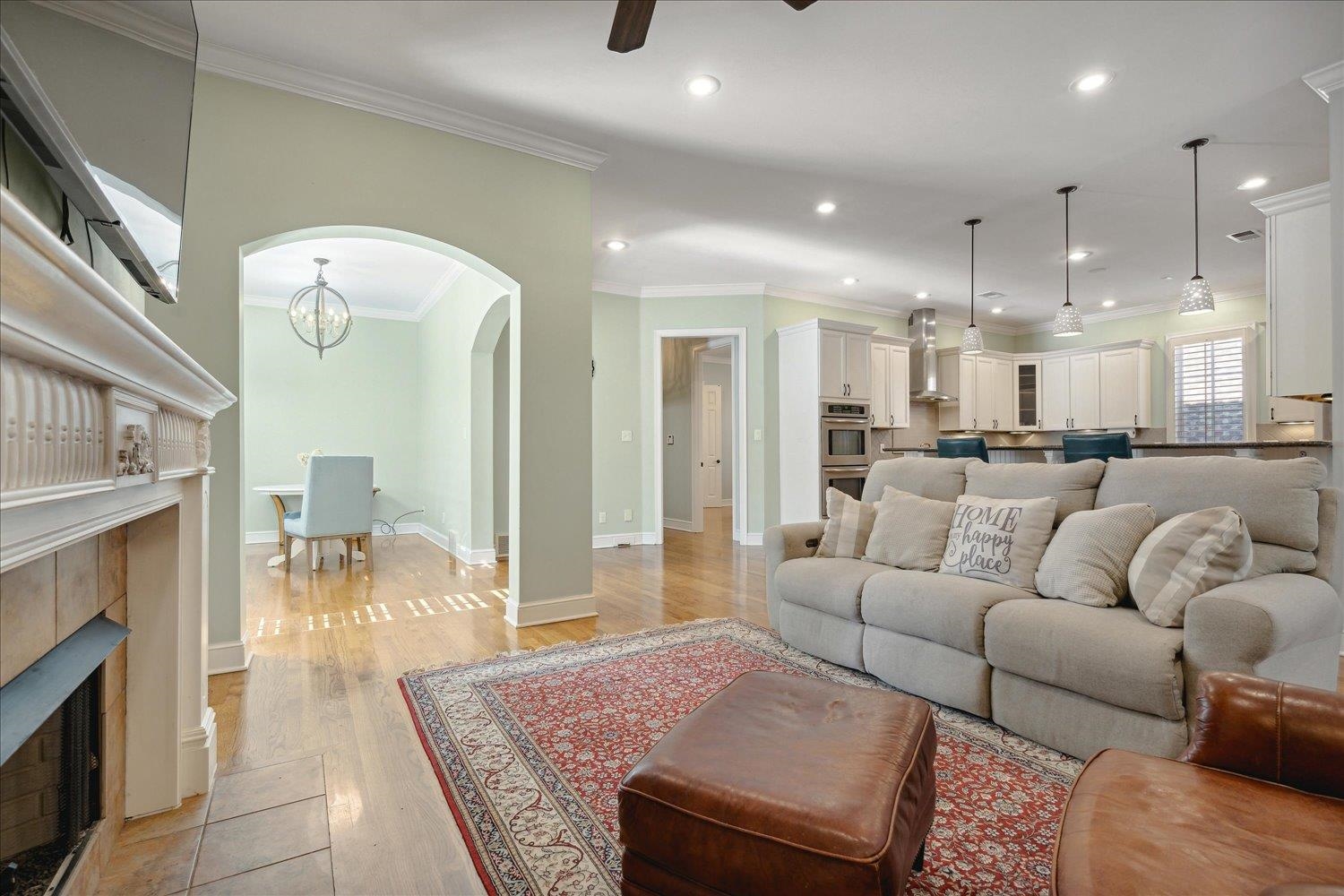 Living room featuring a tiled fireplace, ornamental molding, an inviting chandelier, and light wood-type flooring