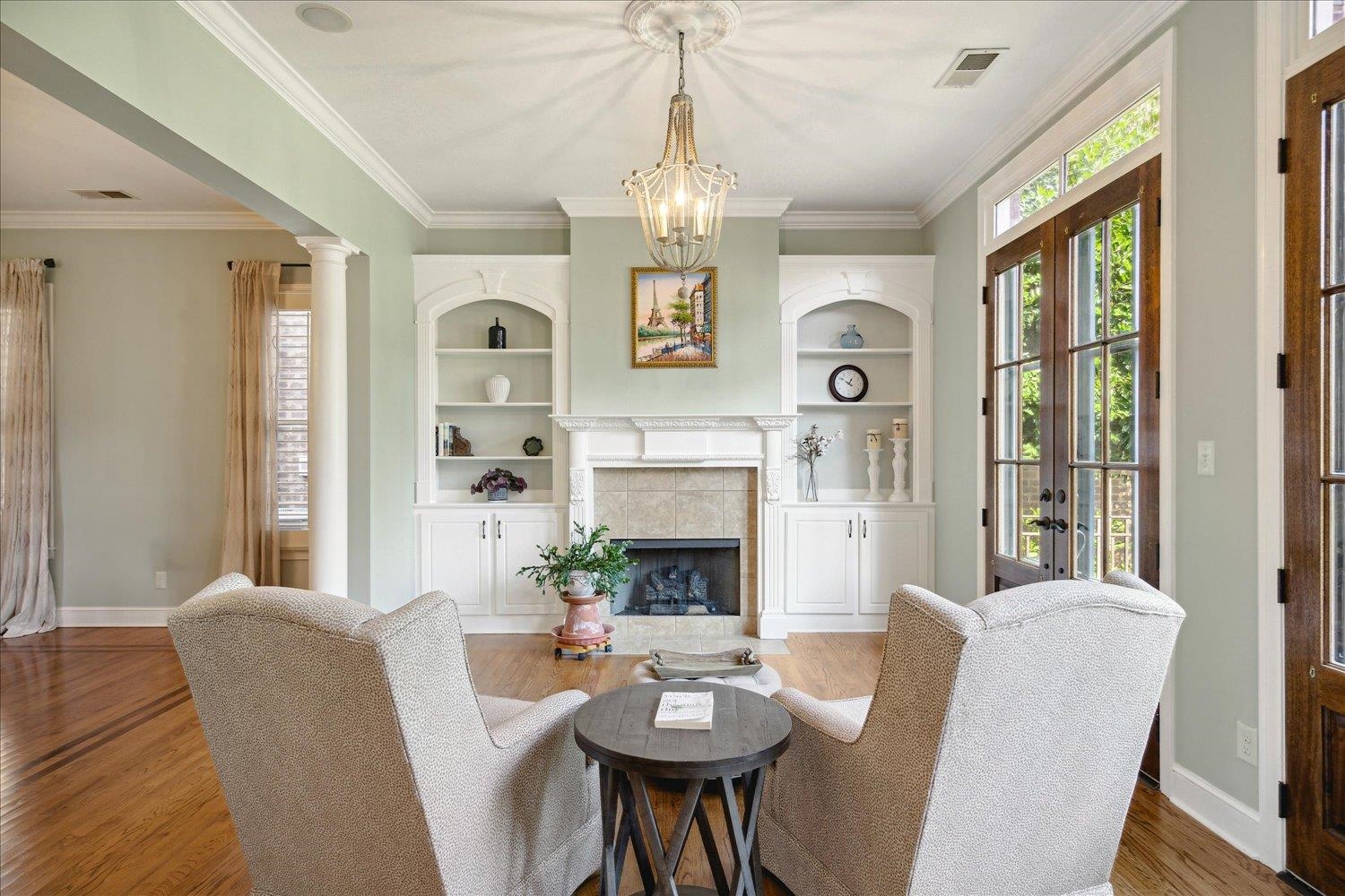 Living room featuring crown molding, a tiled fireplace, wood-type flooring, and built in features