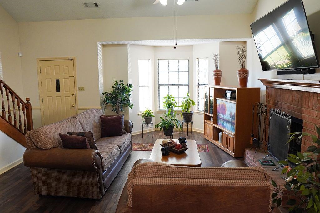 Living room with a healthy amount of sunlight, dark wood-type flooring, ceiling fan, and a brick fireplace