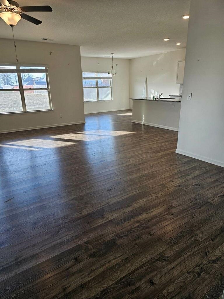 Empty room featuring dark wood-type flooring, a healthy amount of sunlight, a textured ceiling, and ceiling fan with notable chandelier