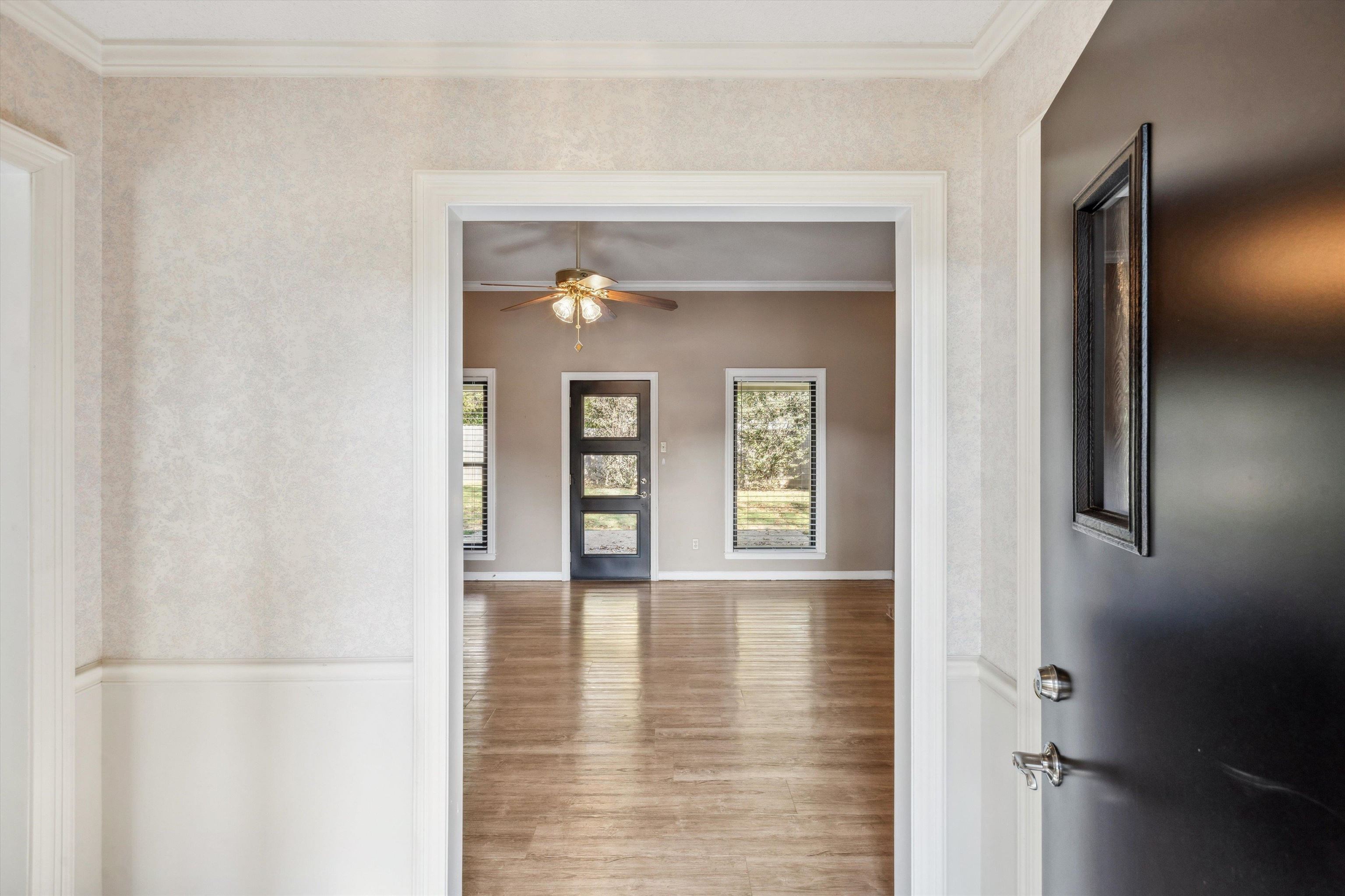 View from the front door of interior space with crown molding, hardwood / wood-style floors, and ceiling fan.