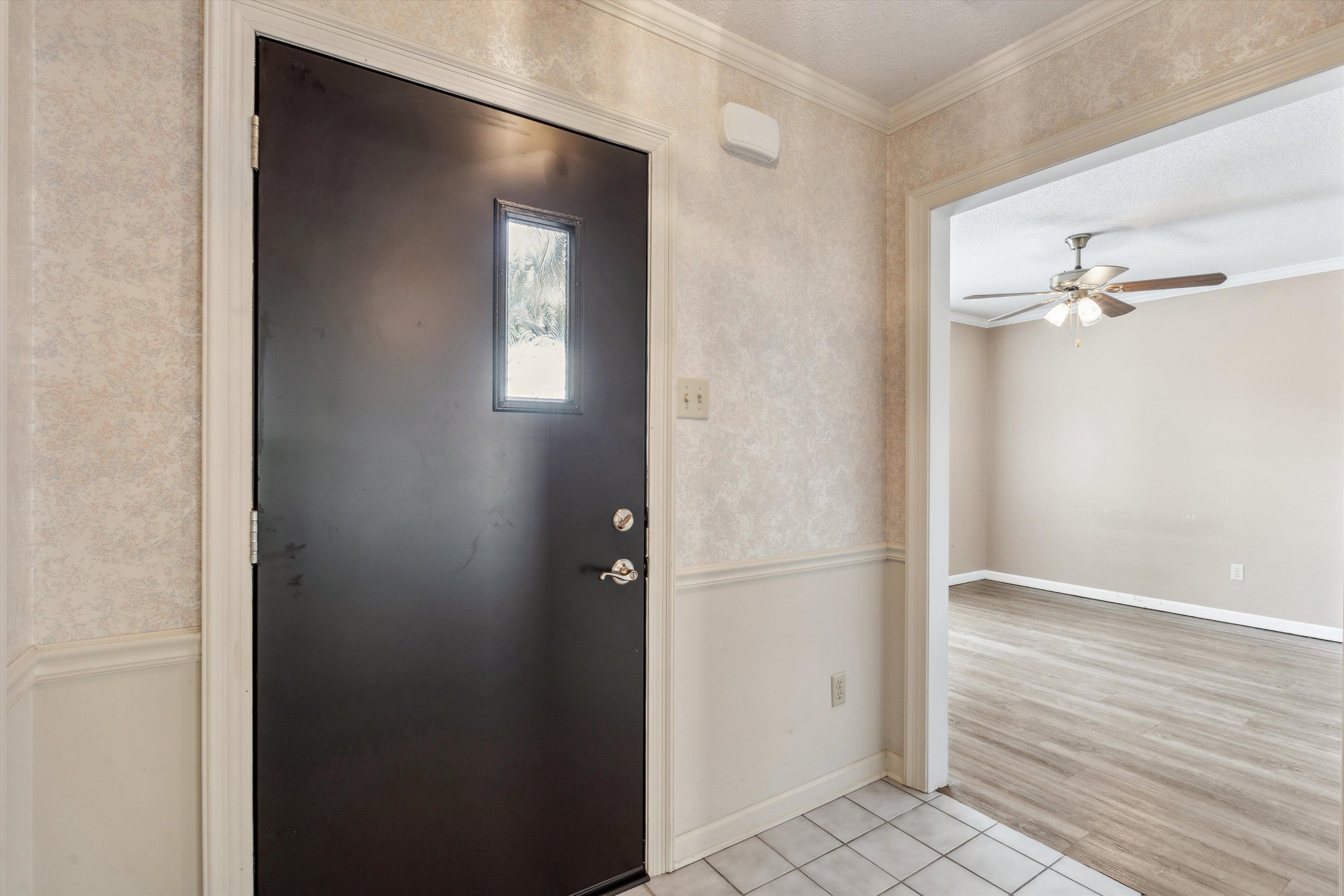 Foyer entrance with crown molding, light hardwood / wood-style flooring, and ceiling fan in the dining room to the left of the entry way after entering the home.